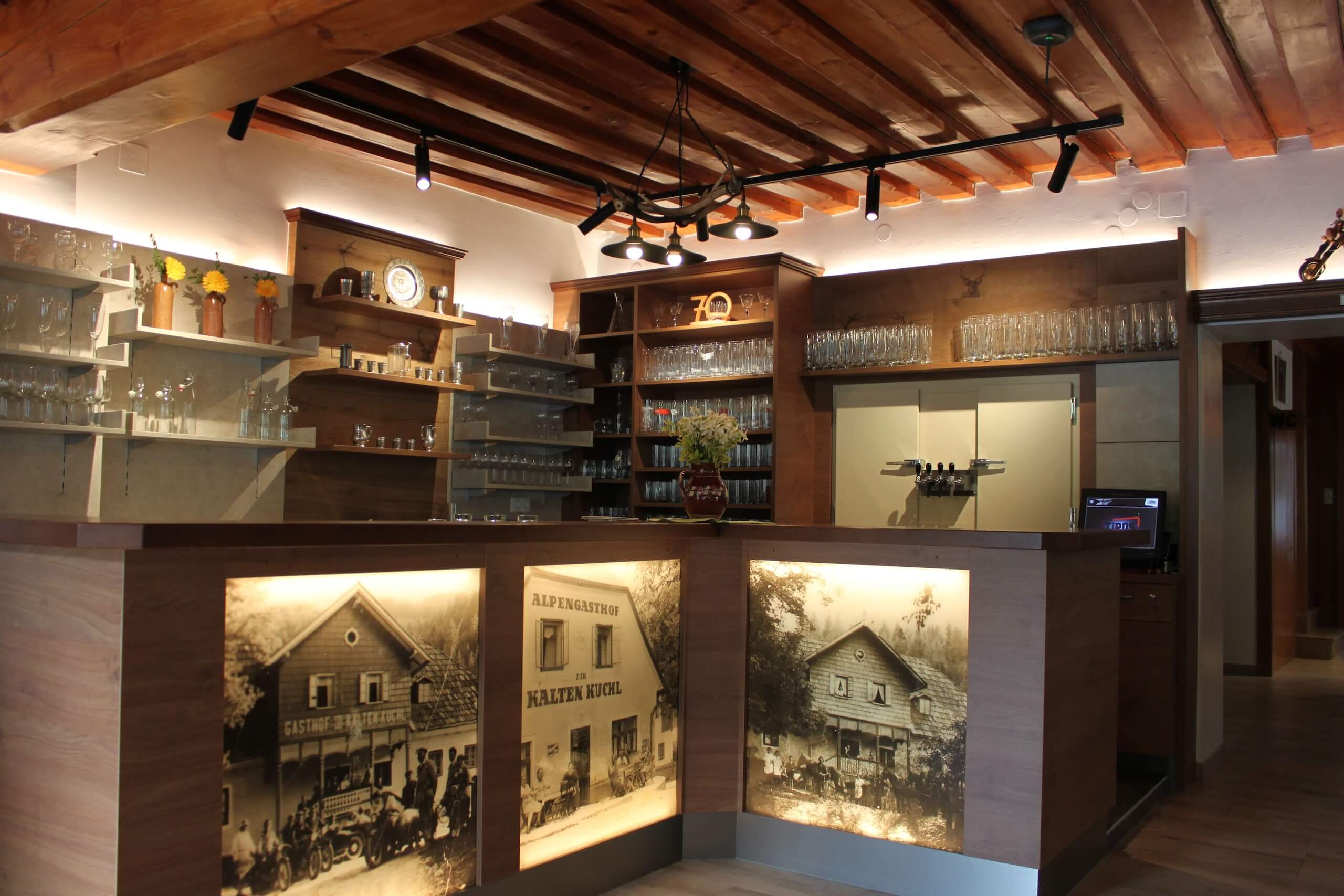 Rustikaler Gasthof-Innenraum mit hölzernem Tresen und antiken Fotografien, ausgestattet mit Gläsern und Zapfhähnen.