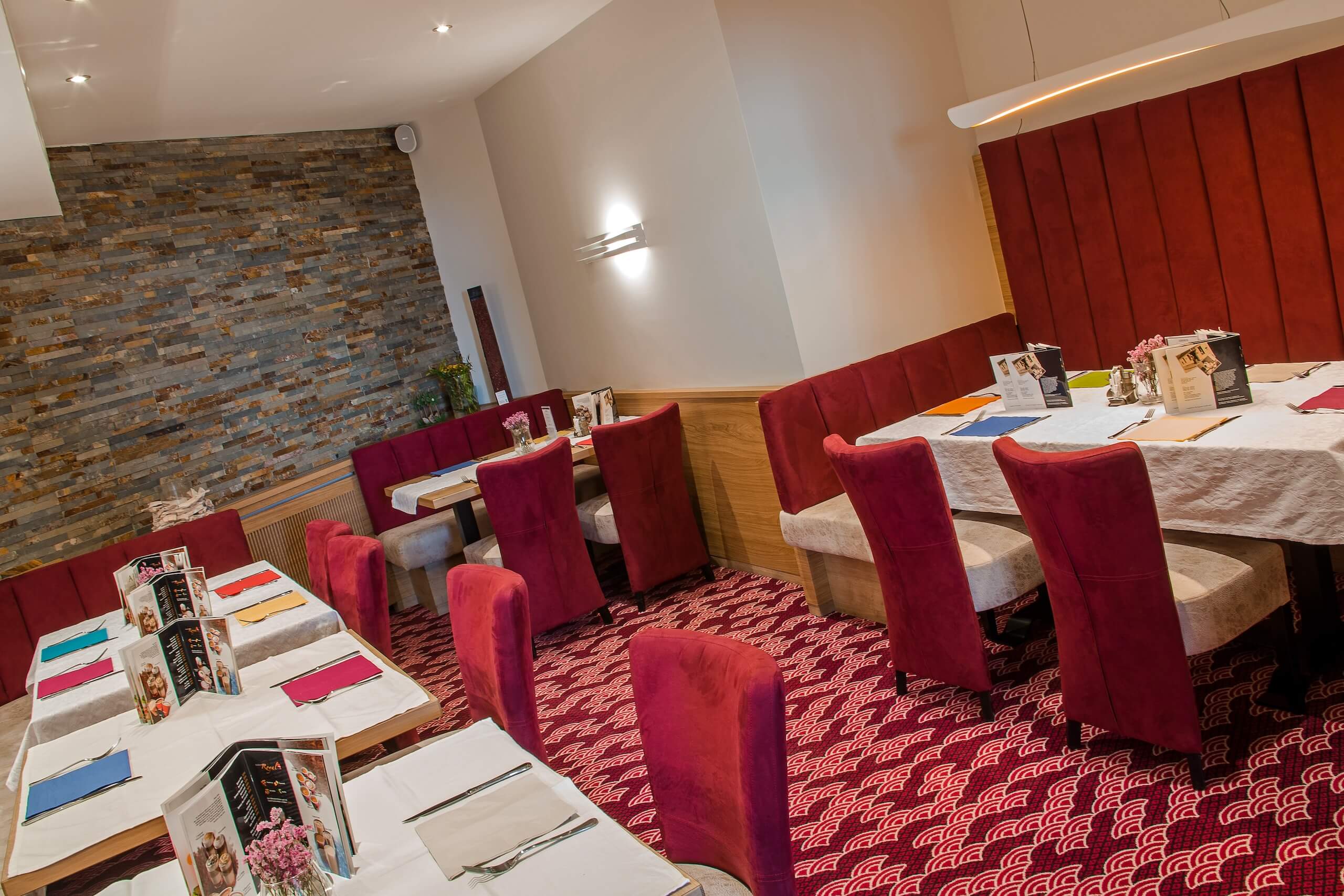 Elegantes Restaurantinterieur mit roten Stühlen, Steinwand und gedeckten Tischen, ideal für ein stilvolles Abendessen.
