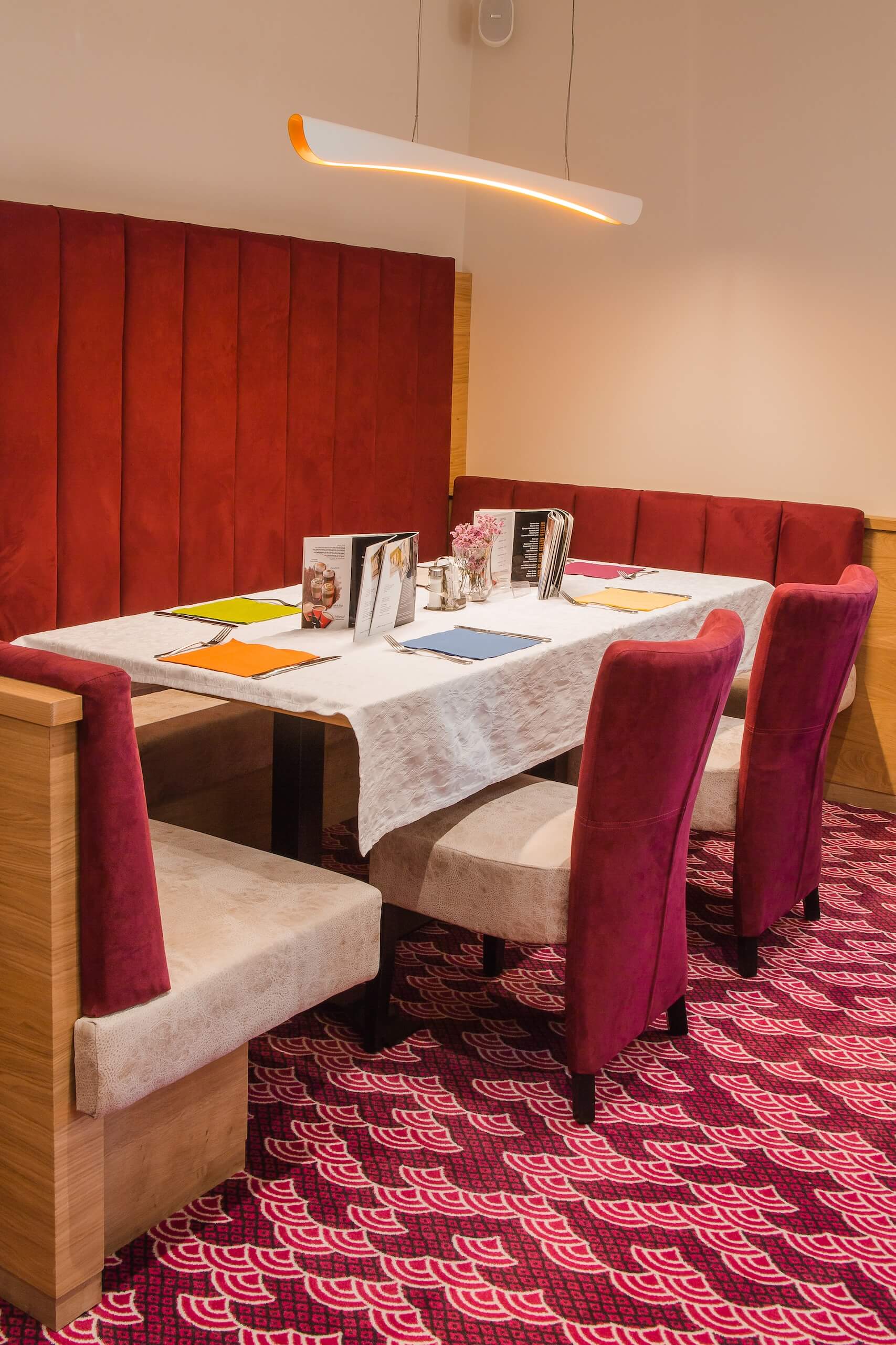 Gemütliche Restaurant-Sitzgruppe mit rotem Polster, dekoriertem Tisch und moderner Beleuchtung.