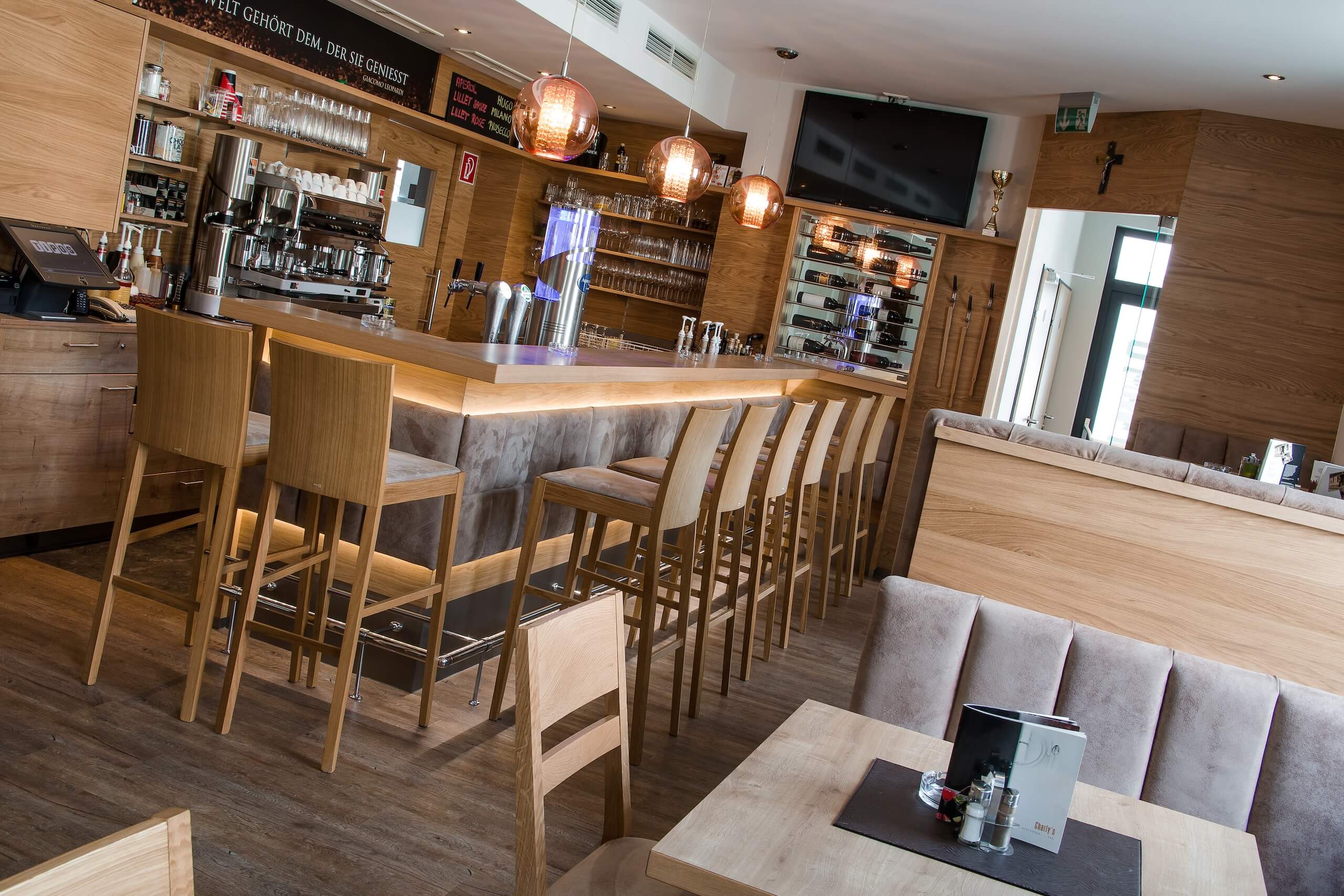 Moderne Bar mit Holzdesign, gemütliche Theke, beleuchtete Flaschenregale und Sitzmöglichkeiten für Gäste.