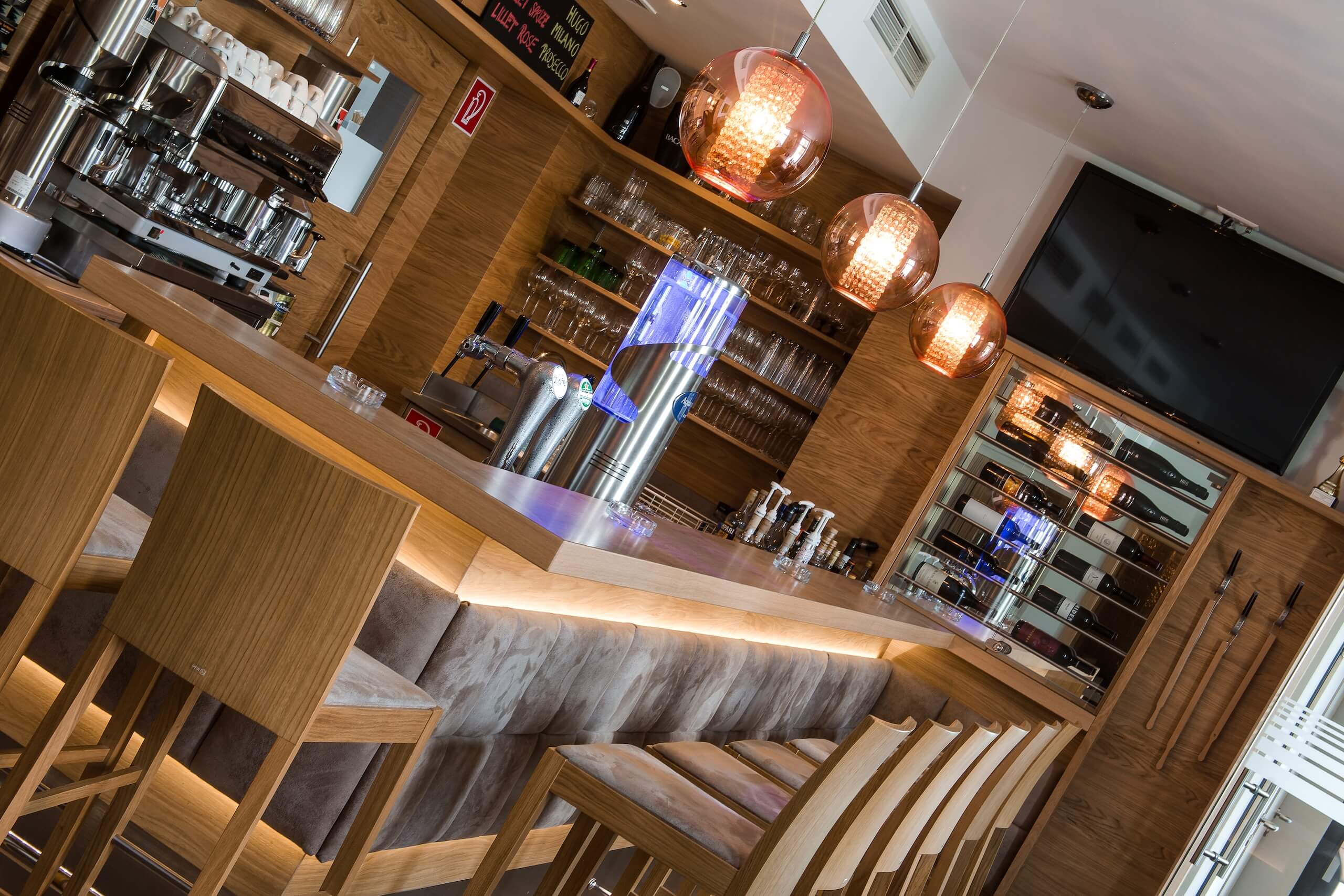 Moderne Bar mit Holzdekor, Hockern, stylischen Lampen und einer Auswahl an Getränken in einer gemütlichen Atmosphäre.