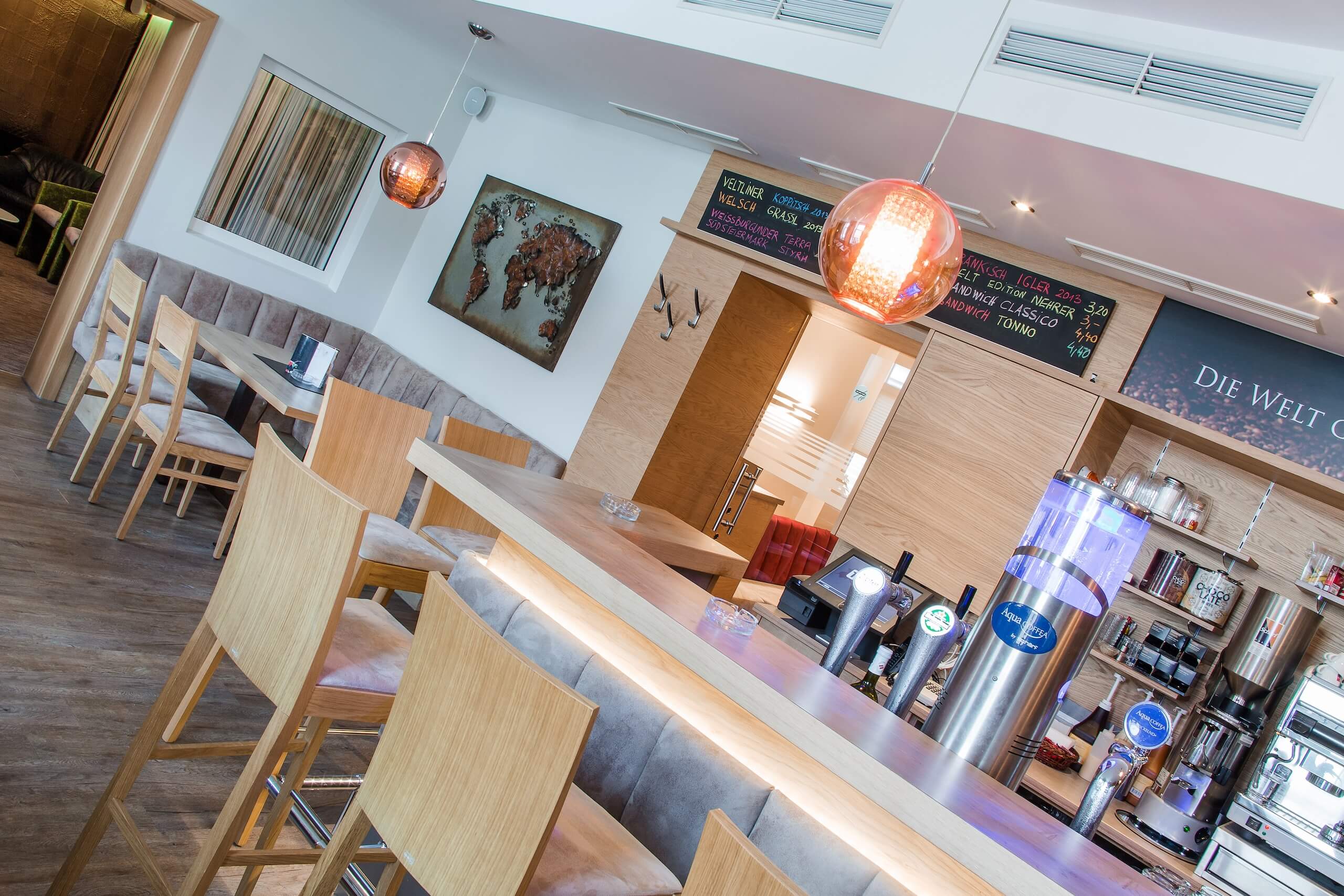 Moderne Bar mit Holzmöbeln, Pendelleuchten und Weltkarte an der Wand, gemütliches Ambiente für Getränke und Treffen.