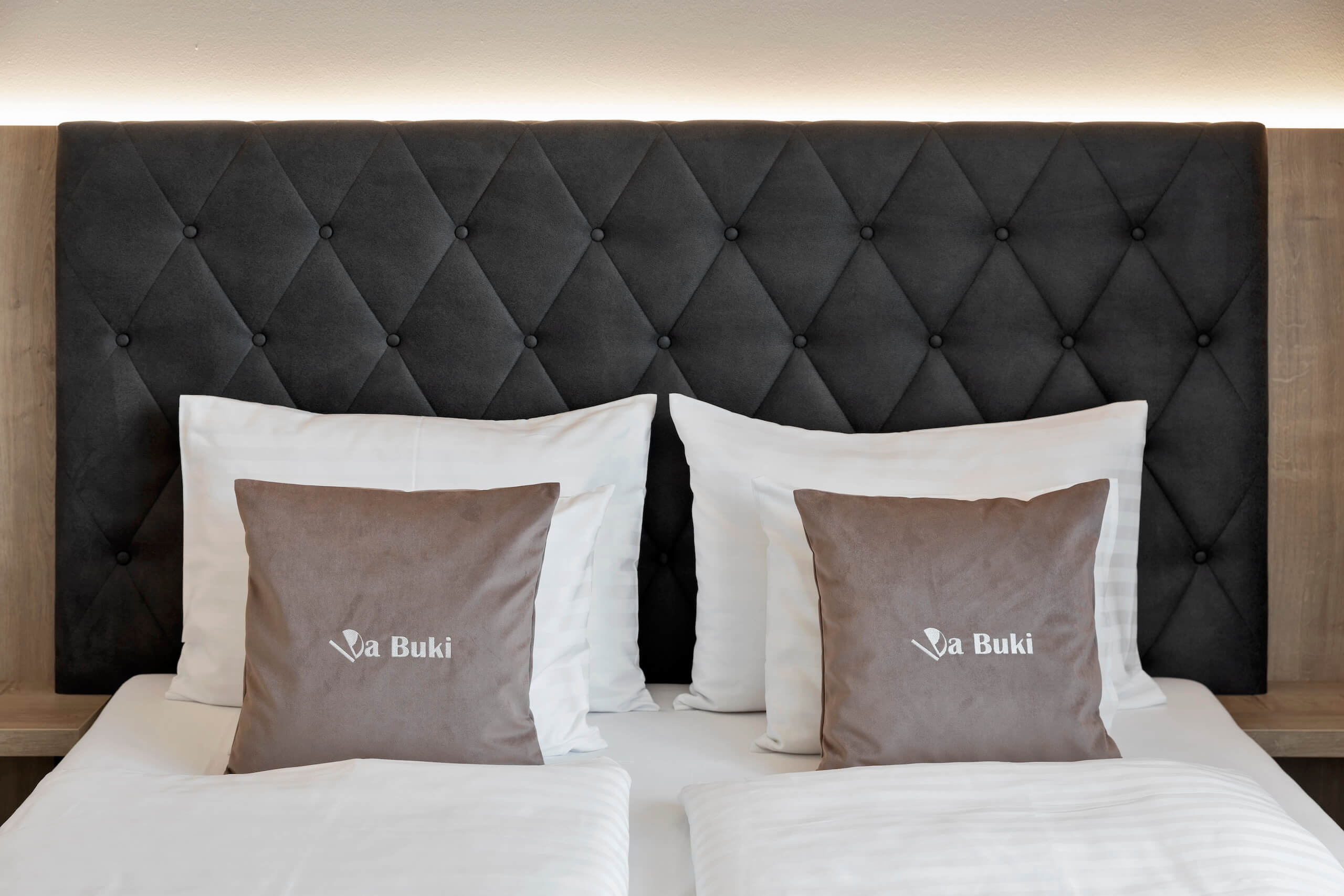 Gemütliches Schlafzimmer mit gepolstertem Kopfteil und dekorativen Kissen, ideal für erholsamen Schlaf im Hotel.