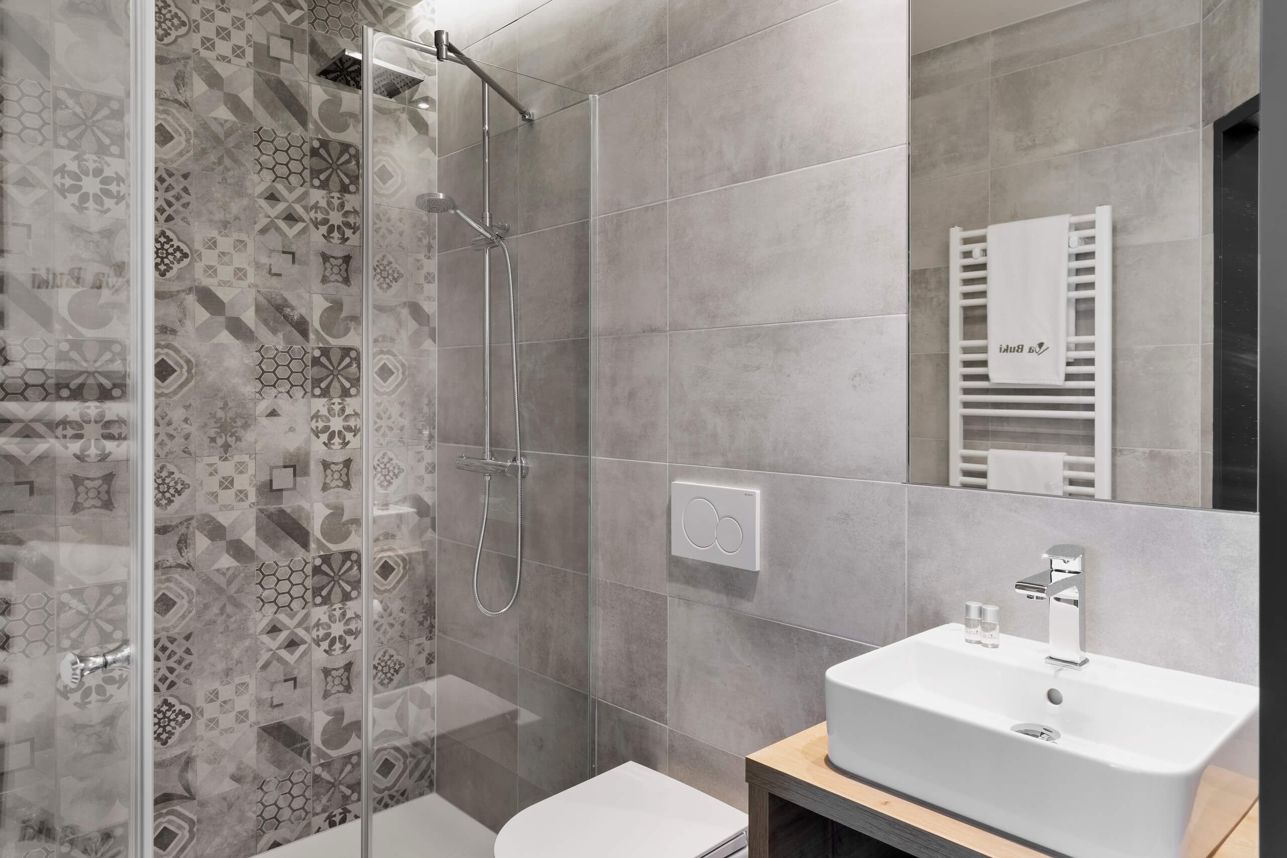 Moderne Badezimmergestaltung mit gemusterten Fliesen, Glasduschkabine und stilvollem Waschbecken vor grauen Wänden.