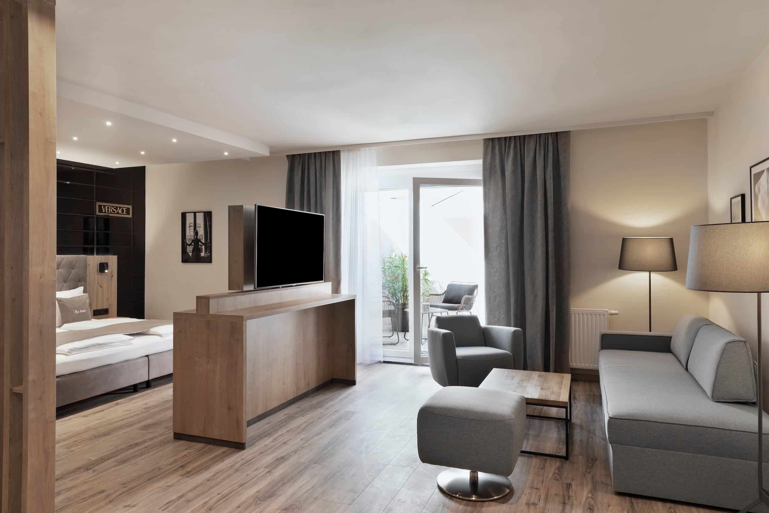 Modernes Wohnzimmer mit grauem Sofa, Flachbild-TV, Holzfußboden und Zugang zu einem Balkon mit Blick auf draußen.