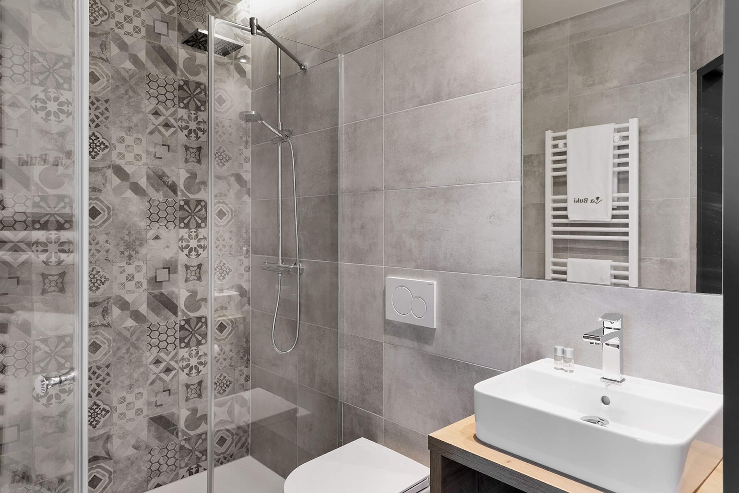 Modernes Badezimmer mit stilvollen grauen Fliesen, Dusche, Waschbecken und Handtuchheizkörper.