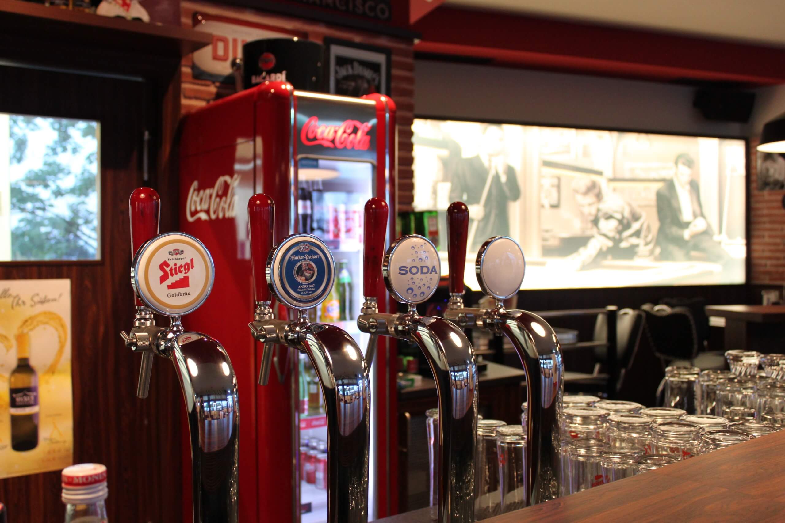Zapfhähne in einer Bar mit einem Coca-Cola-Kühlschrank im Hintergrund. Perfekt für Getränke-Liebhaber.