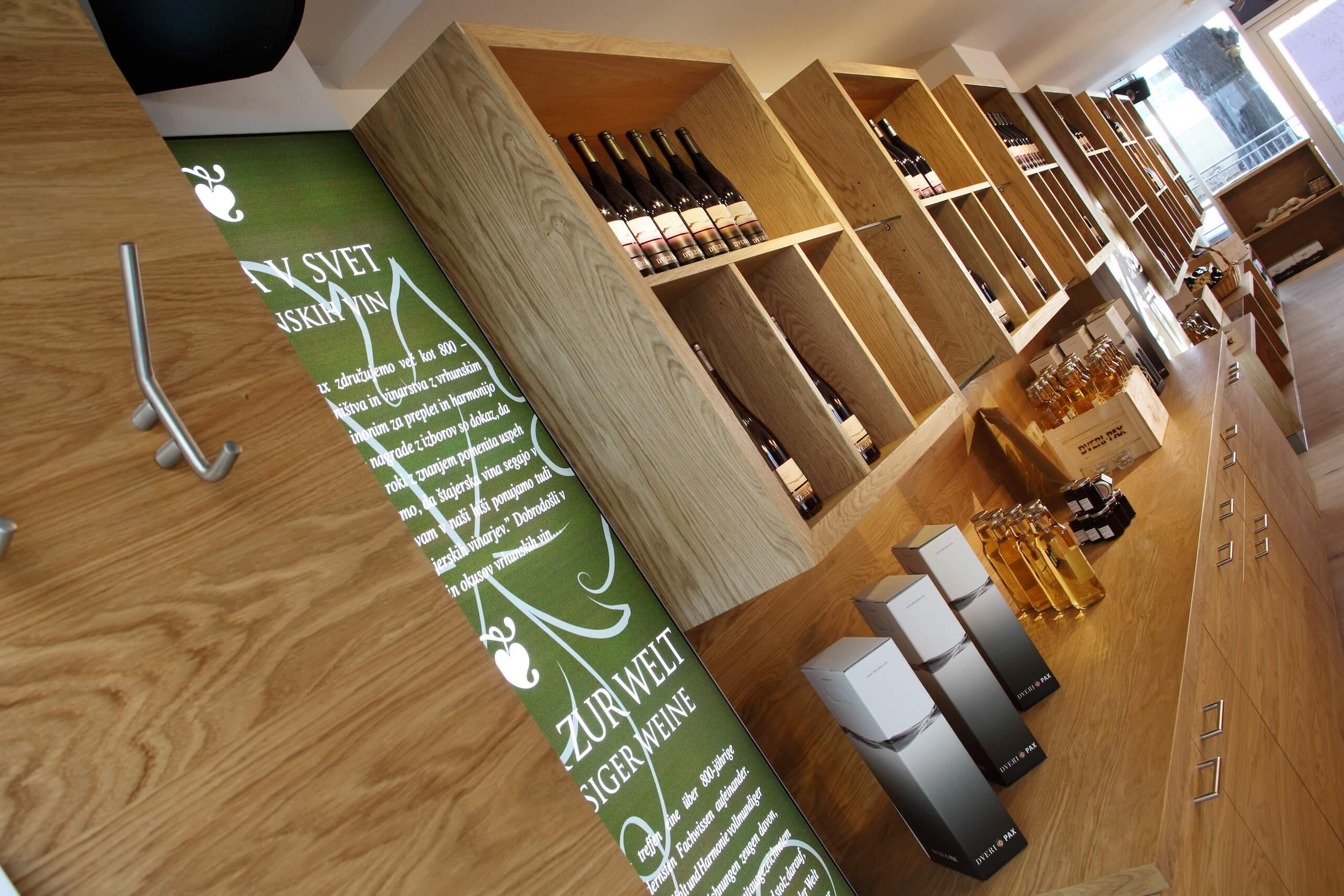 Weinregal in einem Laden, gefüllt mit Weinflaschen und Verpackungen, dekoriert mit einem grünen Info-Panel.