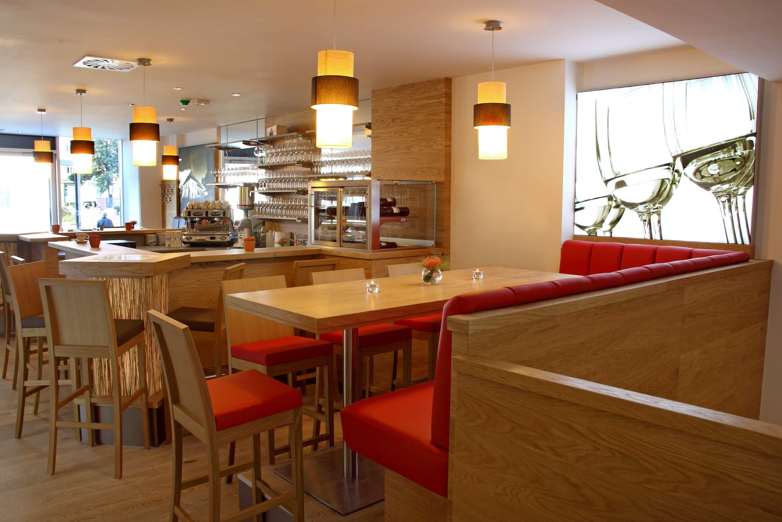 Moderne Café-Inneneinrichtung mit Holzmöbeln, roter Polsterung und stilvollen Hängelampen.