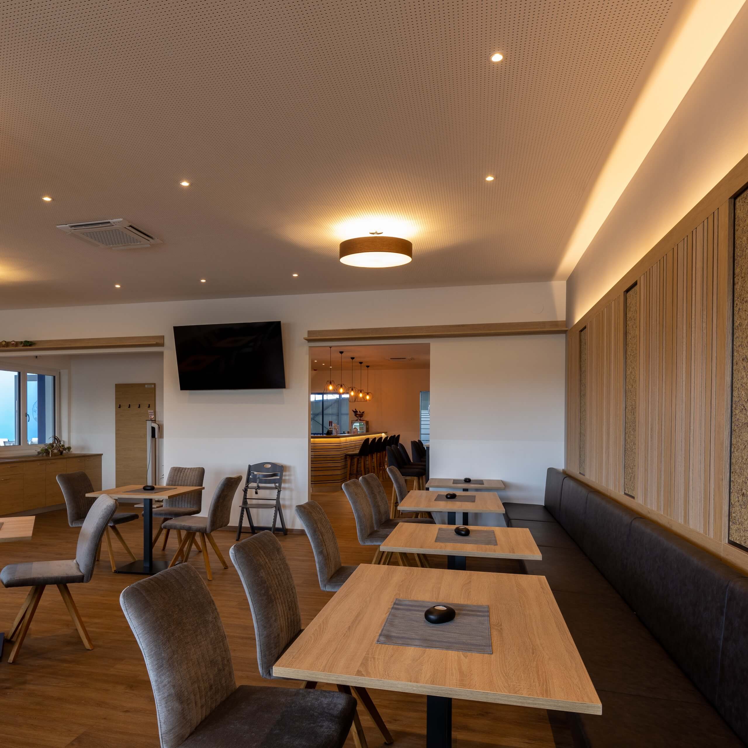 Moderner Speiseraum mit Holztischen und eleganter Beleuchtung, geeignet für stilvolle Restaurant- oder Caféerlebnisse.