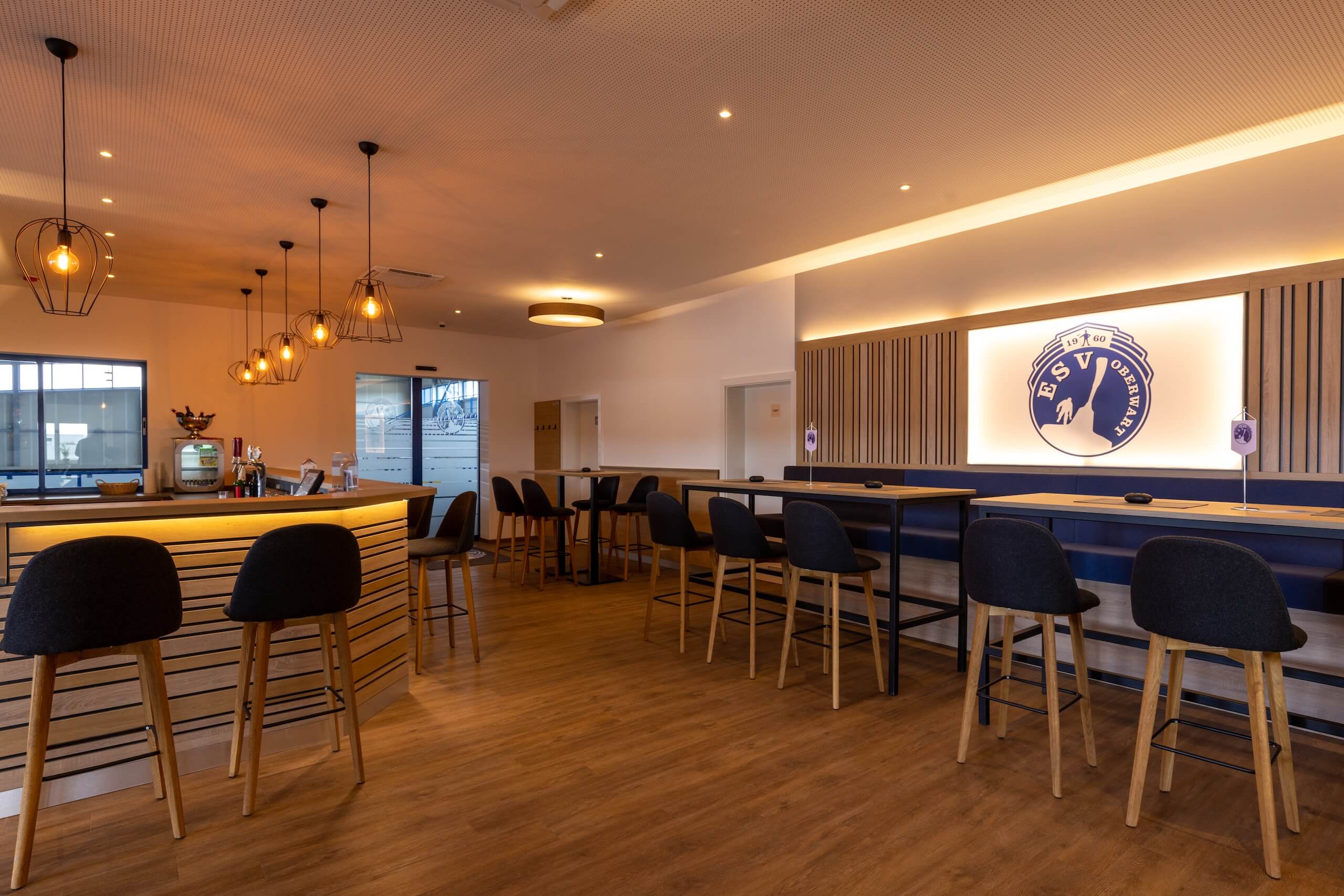 Moderne Bar im Vereinsheim mit stilvoller Beleuchtung und Holzmöbeln, perfekte Umgebung zum Entspannen und Genießen.