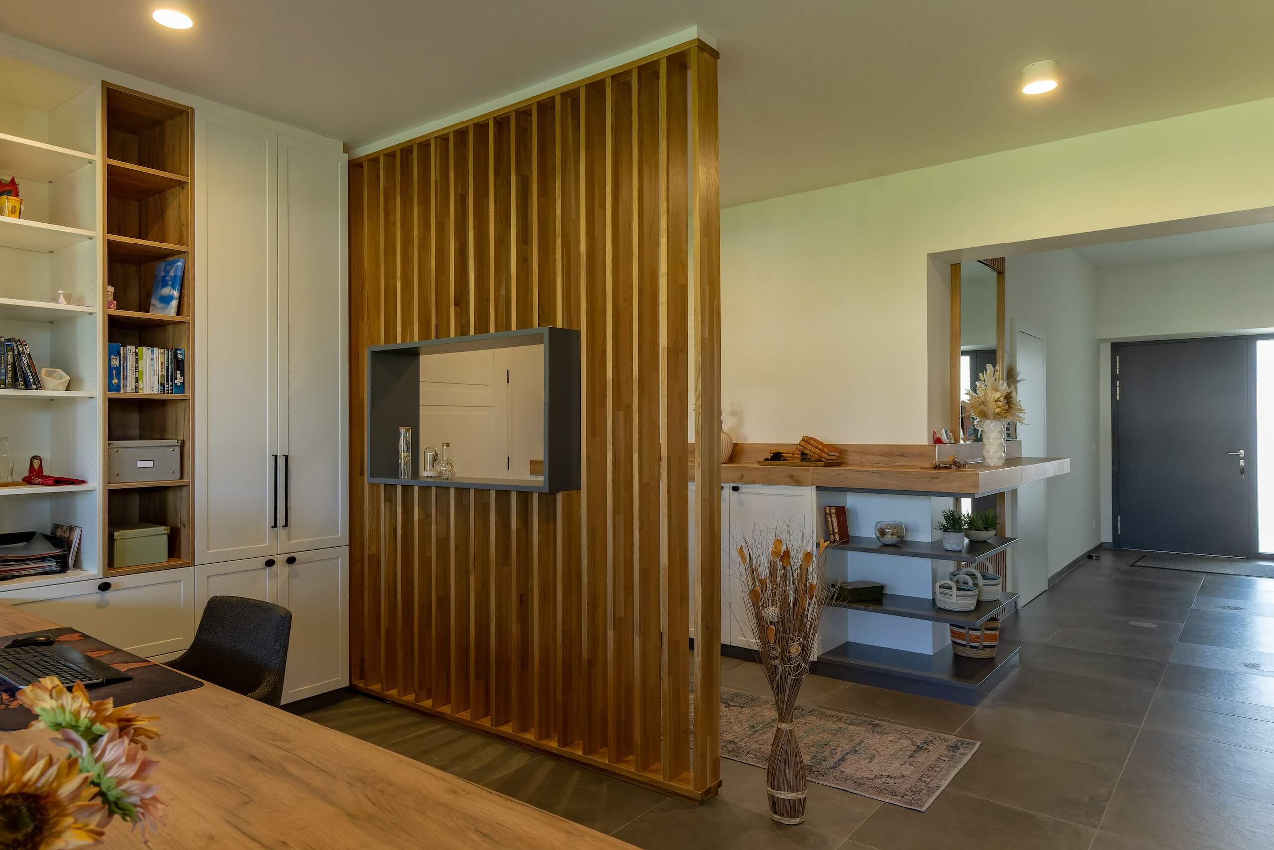 Moderner Innenraum mit Holzwand und offenen Regalen, dekoriert mit Pflanzen und Büchern.