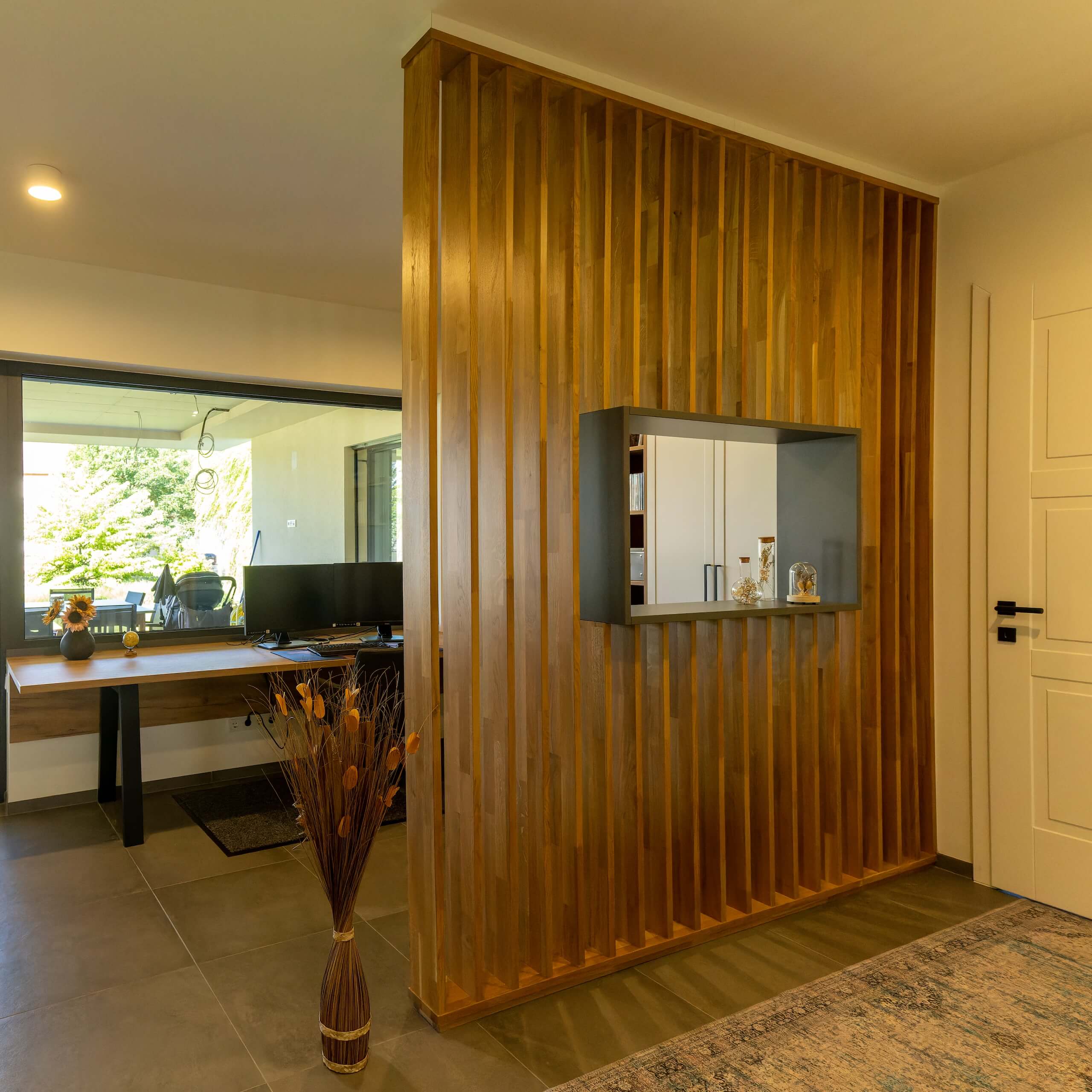 Moderner Raumteiler aus Holz mit integriertem Regal, daneben ein elegantes Homeoffice mit großen Fenster.