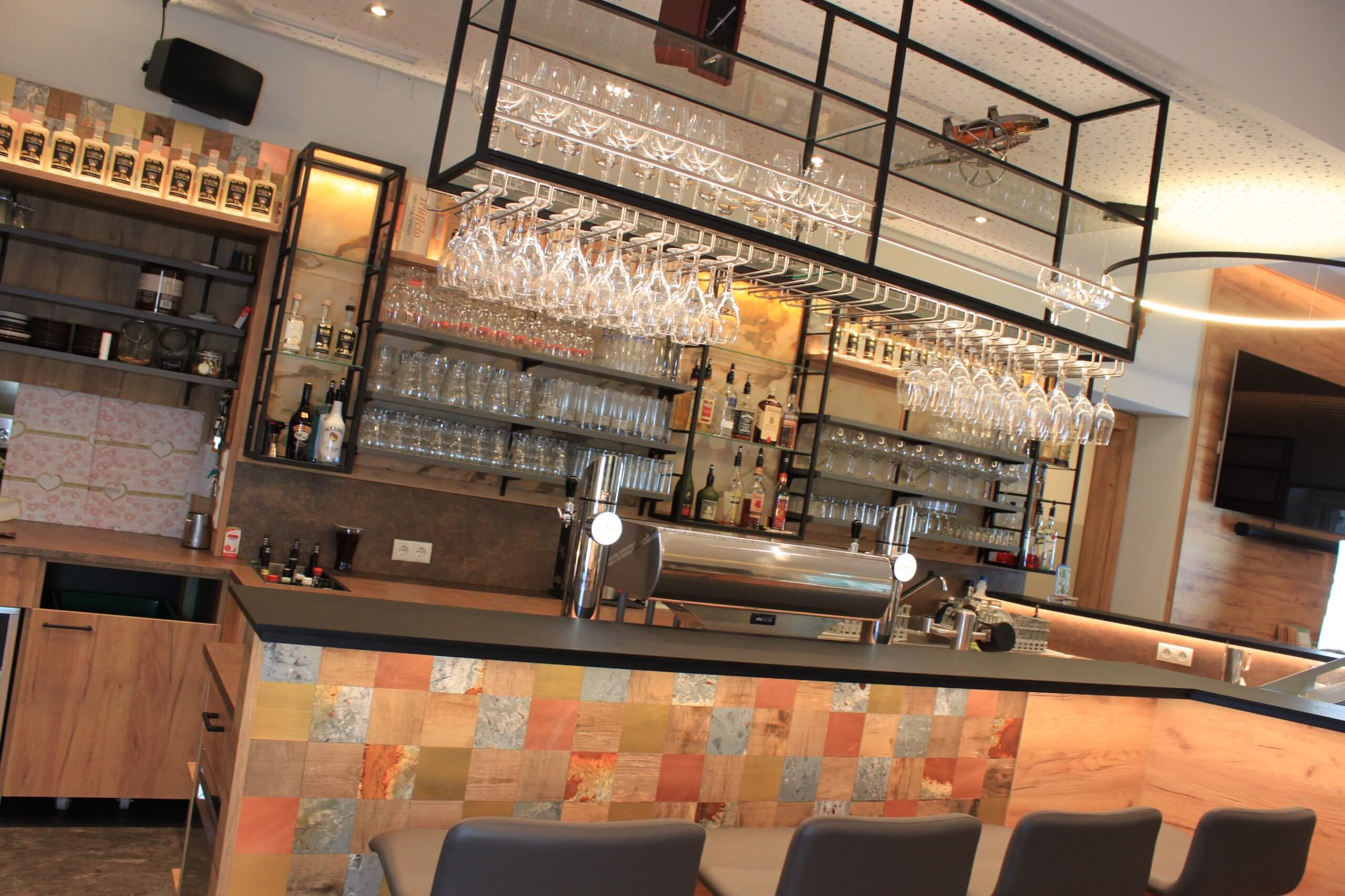 Moderne Bar mit hängenden Gläsern, stilvollem Tresen und bequemen Sitzgelegenheiten für gemütliche Abende.