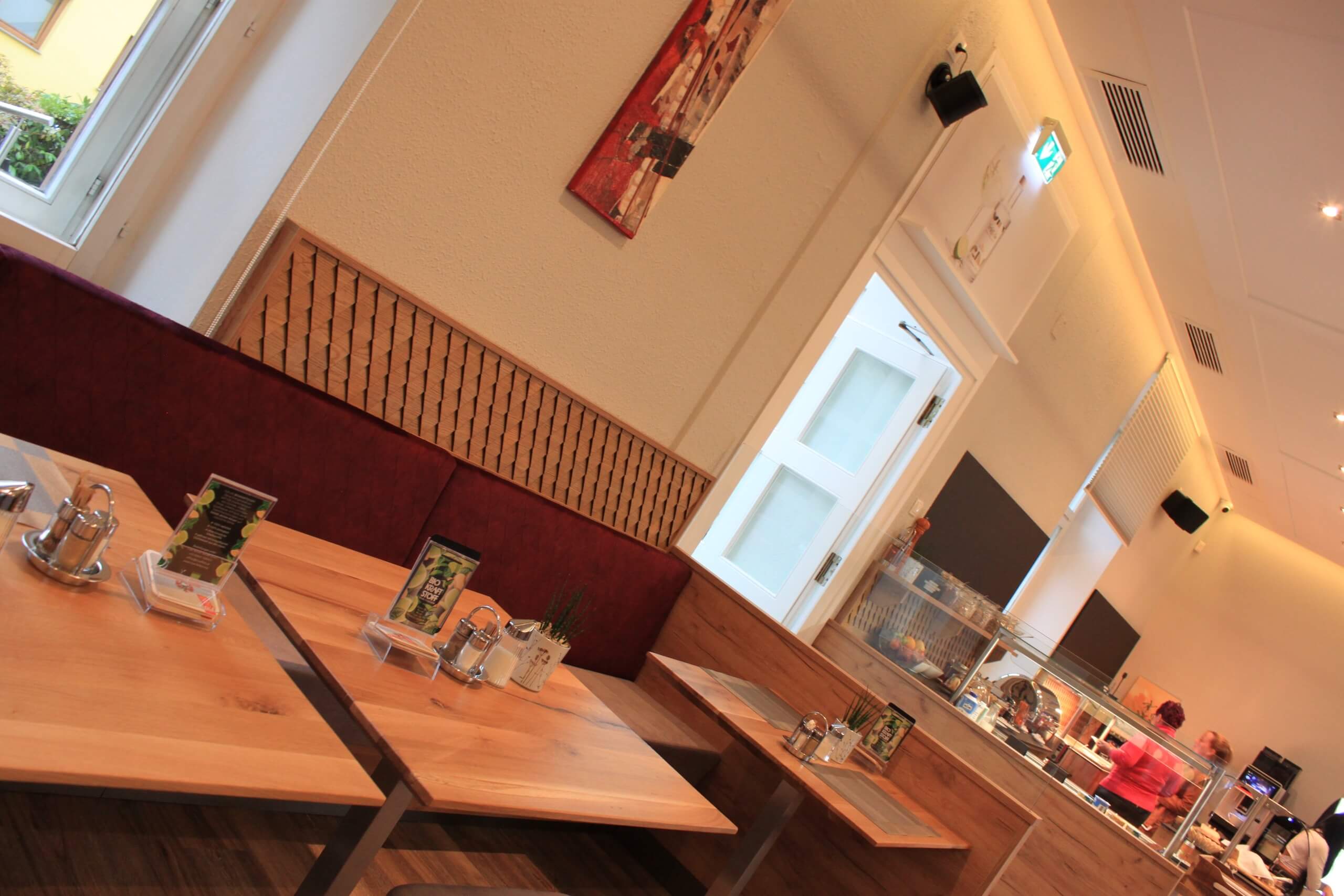 Moderne Cafeteria mit Holztischen, gemütlichen Sitzgelegenheiten und Selbstbedienungsbereich im Innenraum.