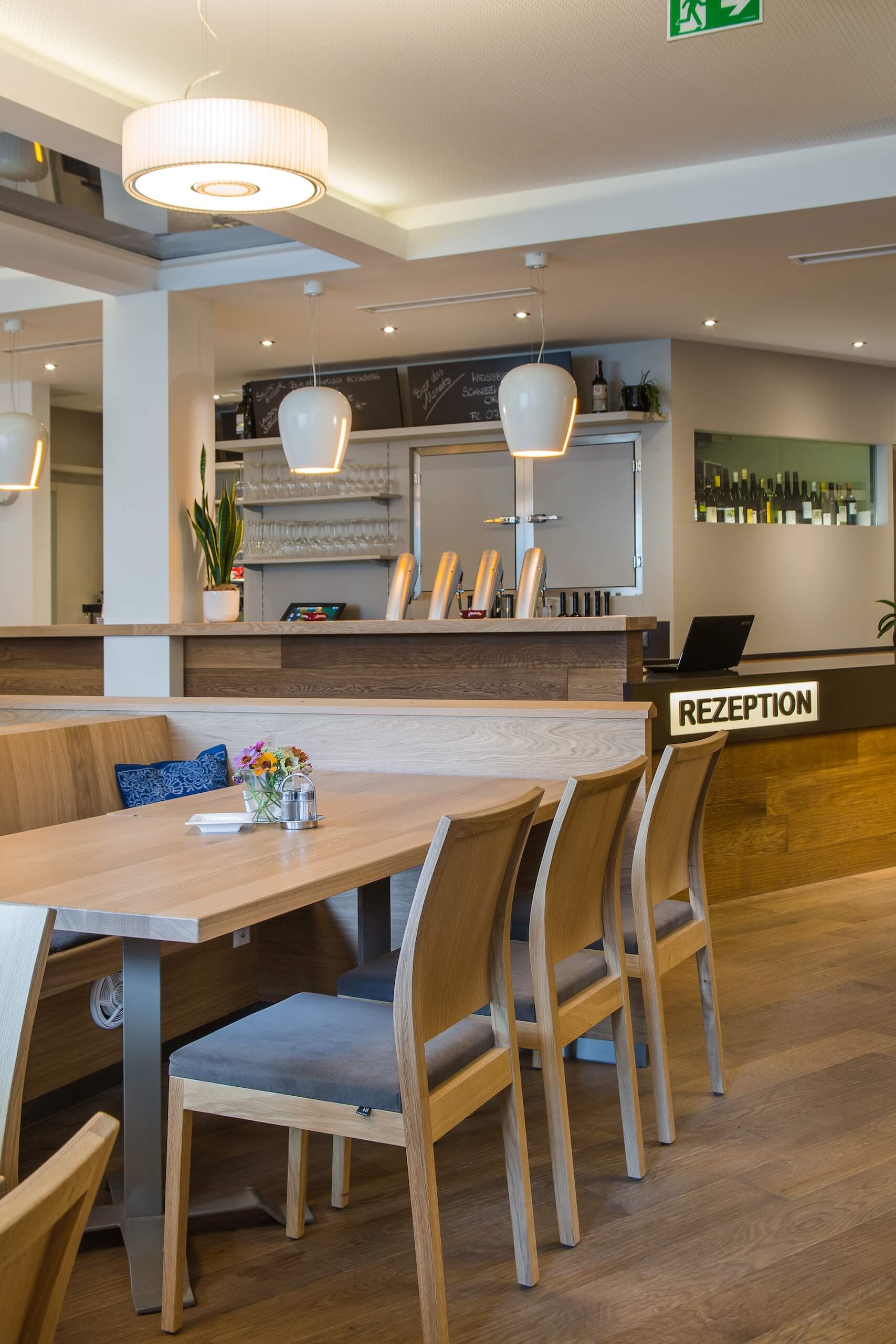 Moderne Hotelrezeption mit Holzdekor, Sitzbereich und beleuchteten Hängeleuchten.