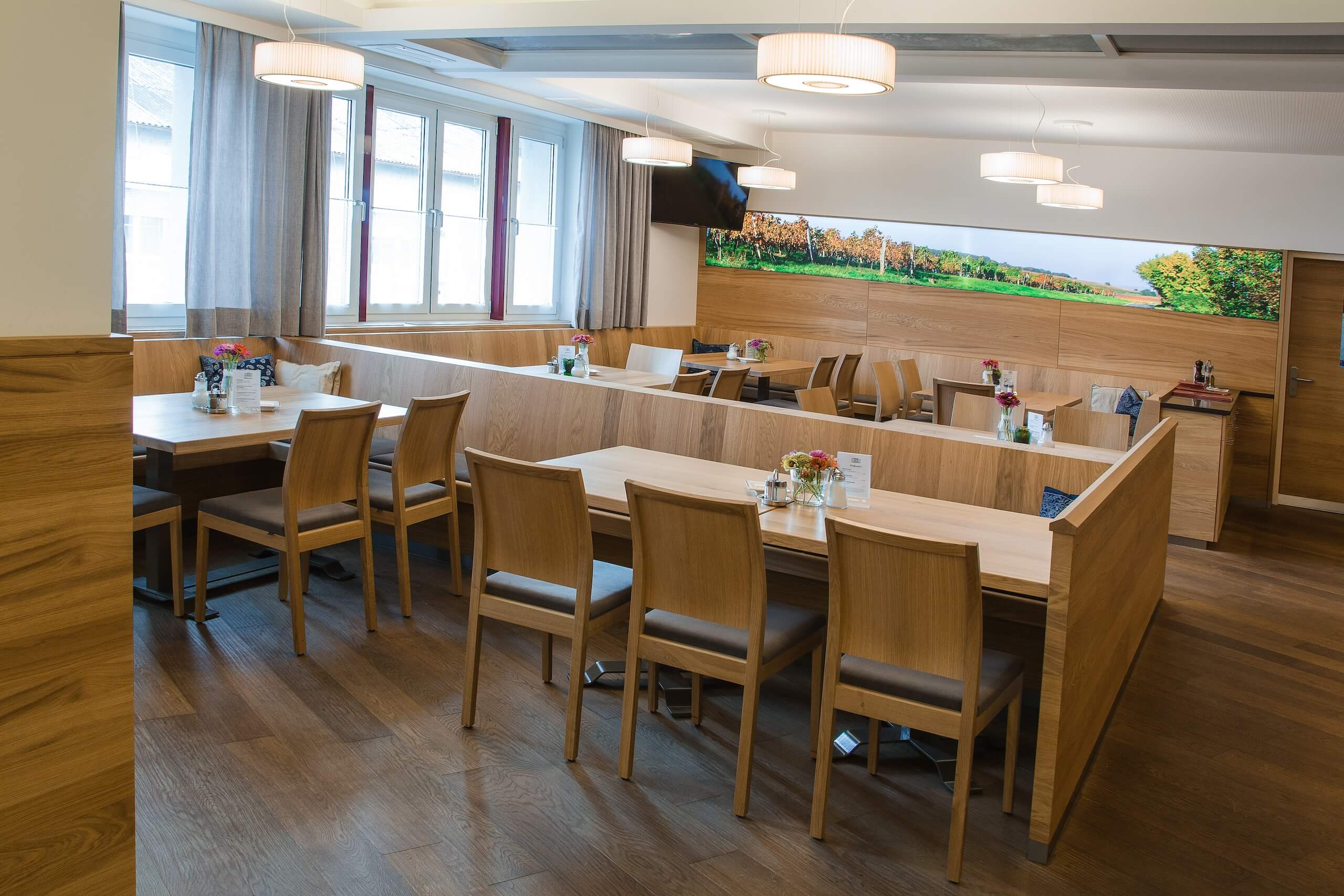 Moderner Gastraum mit Holzmöbeln und Blumenarrangements auf jedem Tisch, ideal für gemütliches Essen und Treffen.