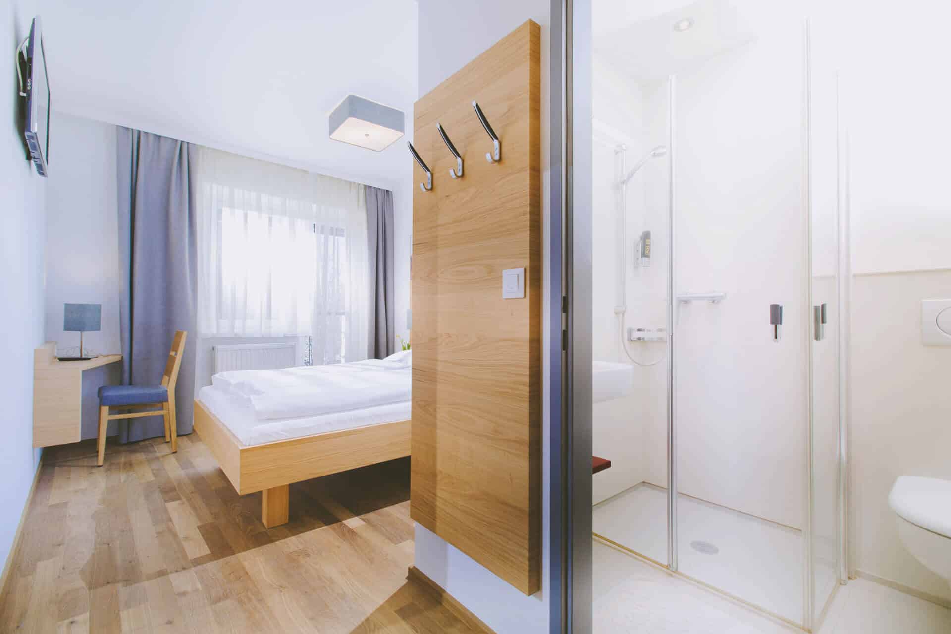 Modernes Hotelzimmer mit Holzfußboden, großem Fenster, Doppelbett und eigenem Bad mit Dusche.
