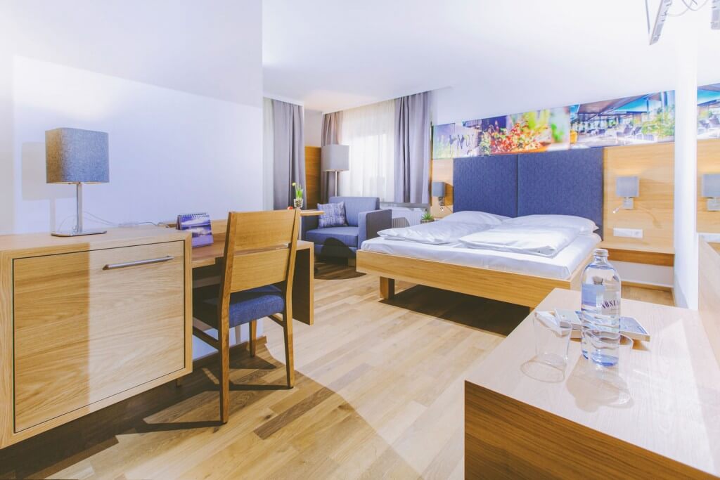 Modernes Hotelzimmer mit Holzdekor, Doppelbett und Schreibtisch. Helle, einladende Atmosphäre für erholsamen Aufenthalt.
