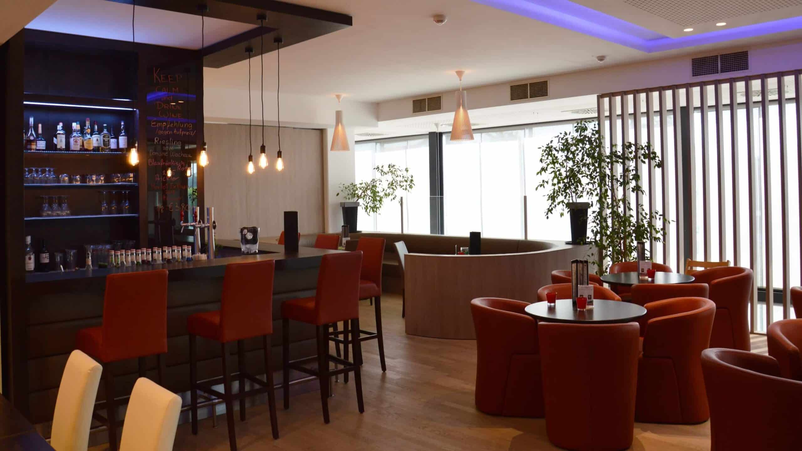Moderne Hotelbar mit stilvollen roten Stühlen und eleganter Beleuchtung für eine entspannte Atmosphäre.