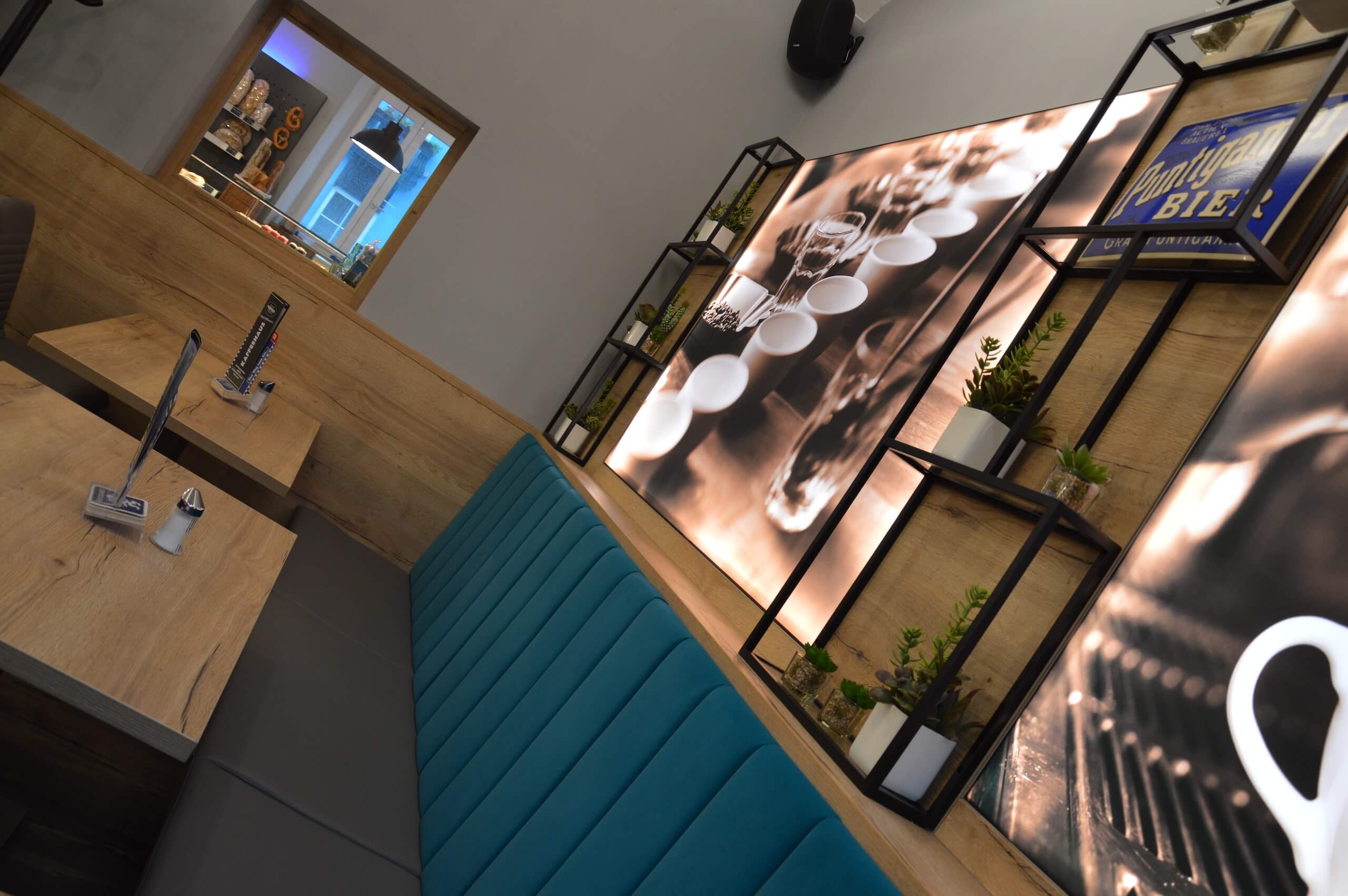 Moderne Café-Inneneinrichtung mit stilvollen Holzmöbeln und beleuchteten Wandbildern, blau gepolsterte Sitzbank.