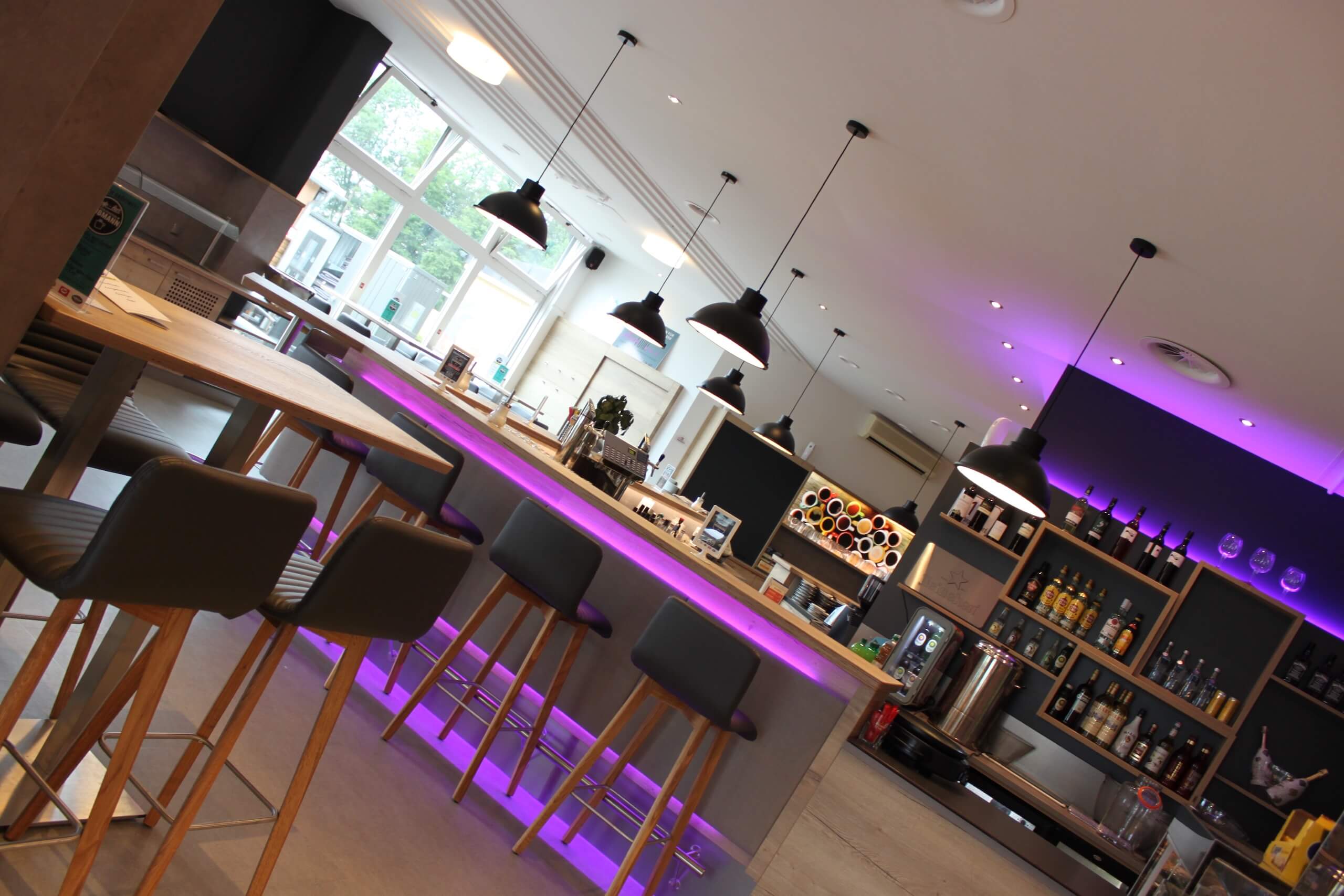 Stylishe Bar mit modernen Hockern, stimmungsvoller Beleuchtung und gut bestückten Regalen für Getränke in warmem Ambiente.