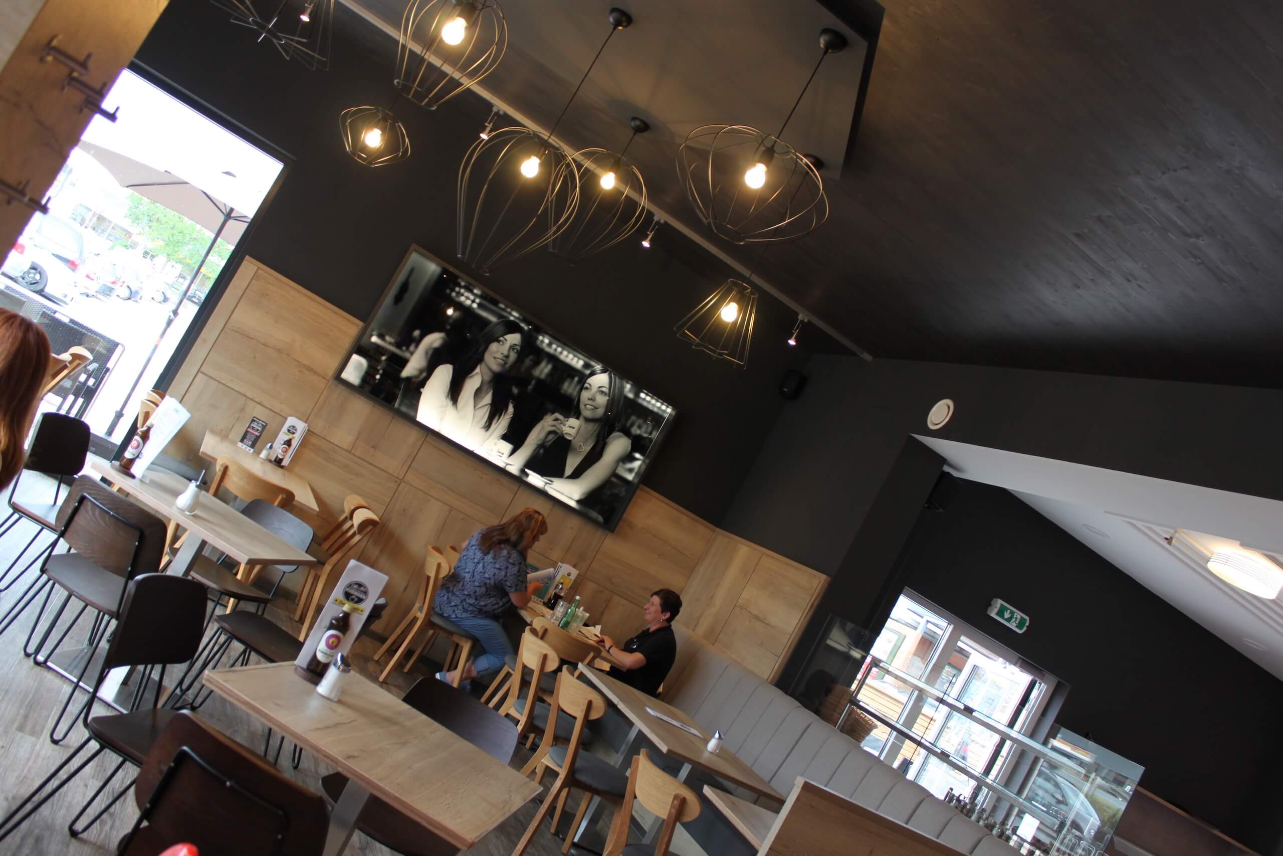 Moderner Café-Innenraum mit stilvoller Beleuchtung und Gästen, die an Holztischen sitzen.