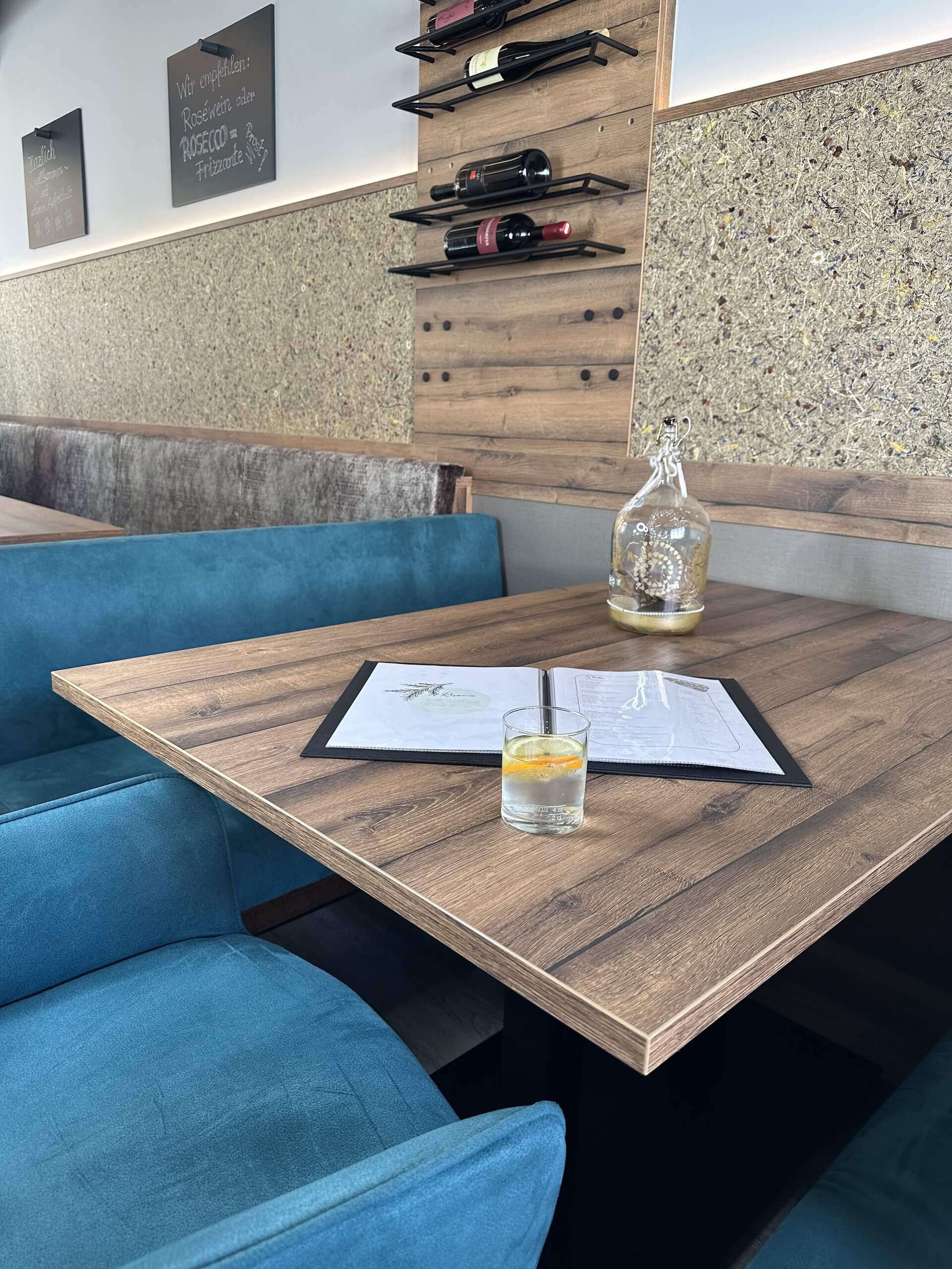 Gemütliche Restaurant-Ecke mit Holztisch, Menü, Getränk und Weinregal an der Wand für einladende Atmosphäre.