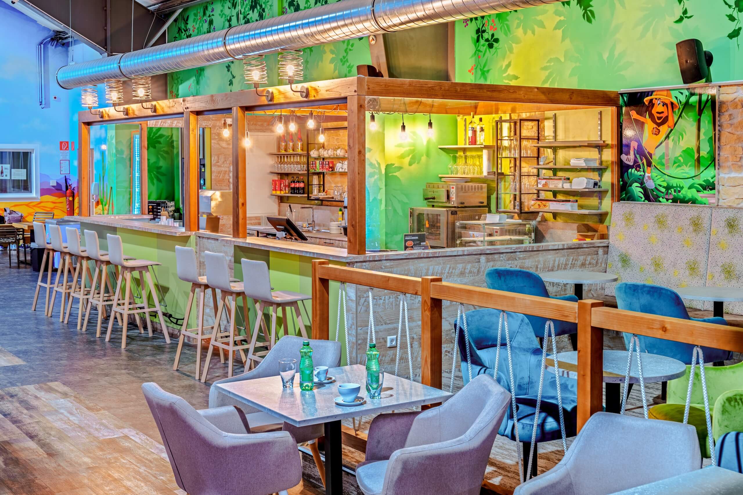 Moderne Café-Bar mit grüner Wanddekoration, Holzstühlen und gemütlichen Sitzbereichen für entspanntes Ambiente.