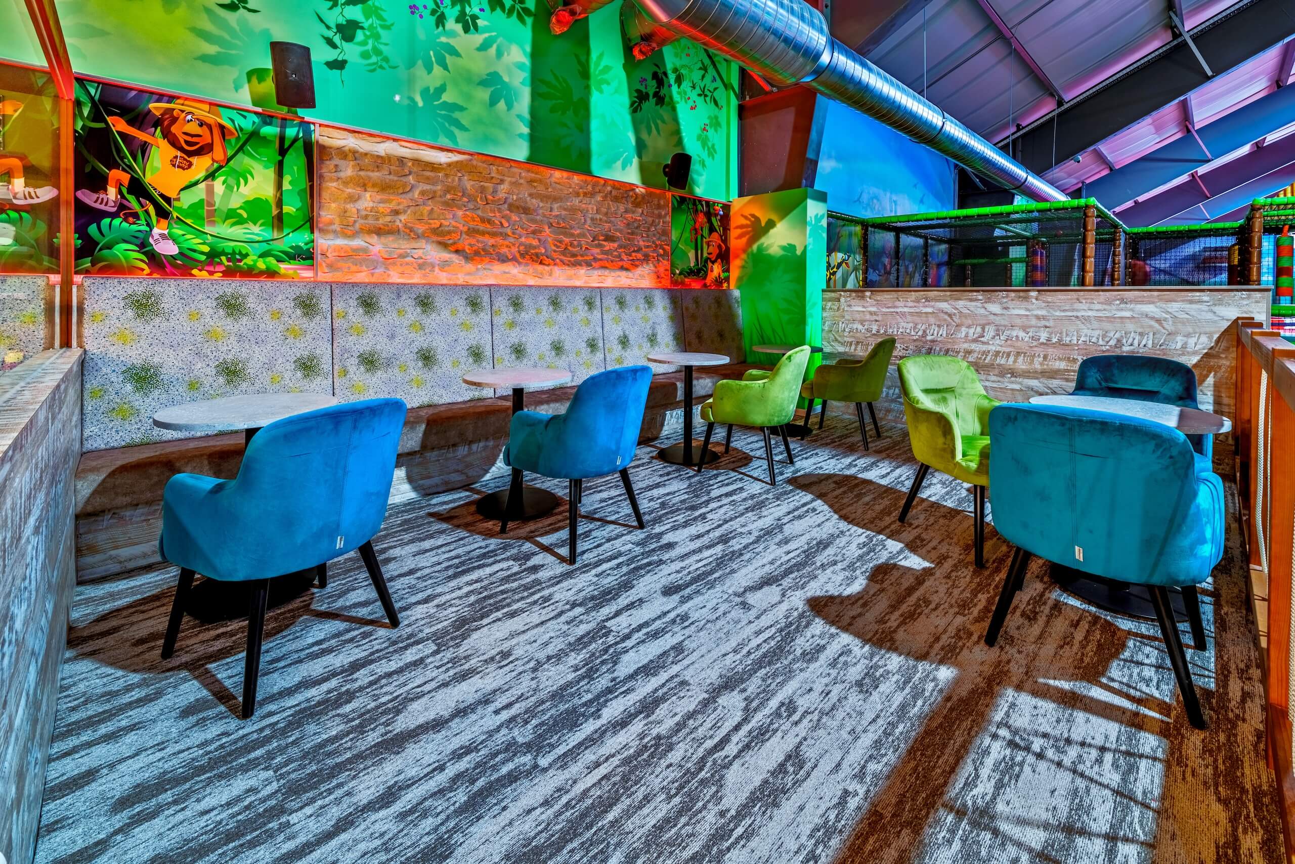 Bunte Indoor-Spielplatz-Lounge mit blauen und grünen Stühlen, leuchtendem Dschungel-Thema und gemütlicher Atmosphäre.
