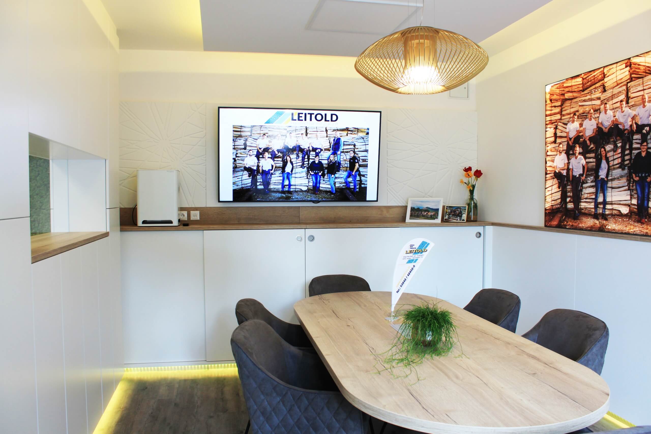 Moderner Besprechungsraum mit Holztisch, Leinwand und dekorativer Beleuchtung für kreative Meetings.