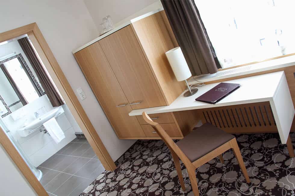 Modernes Hotelzimmer mit Schreibtisch, Holzmöbeln und angrenzendem Badezimmer für komfortable Übernachtungen.