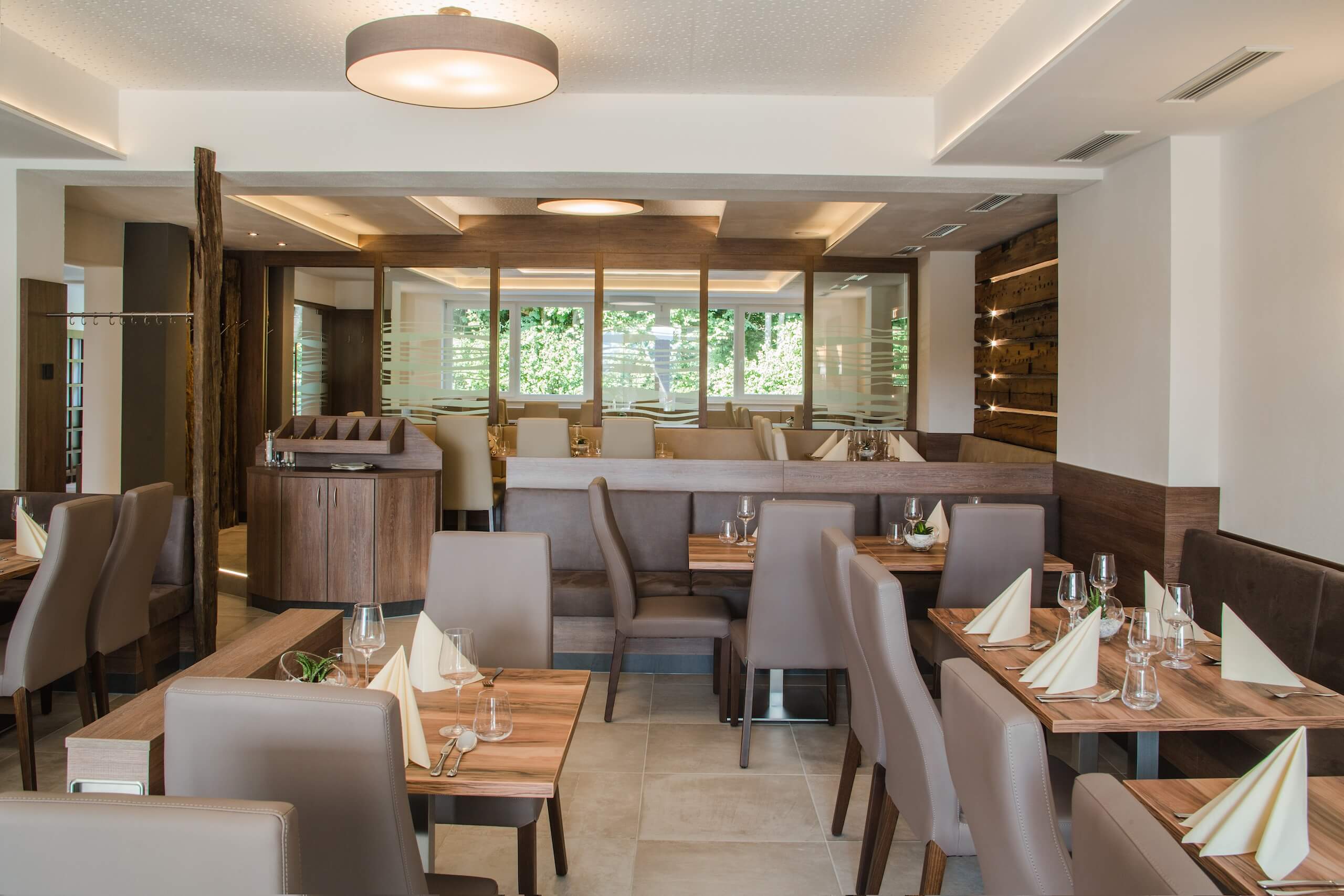 Modernes Restaurantinterior mit gedeckten Holztischen und Ledersesseln, stilvolles Ambiente für Gäste.