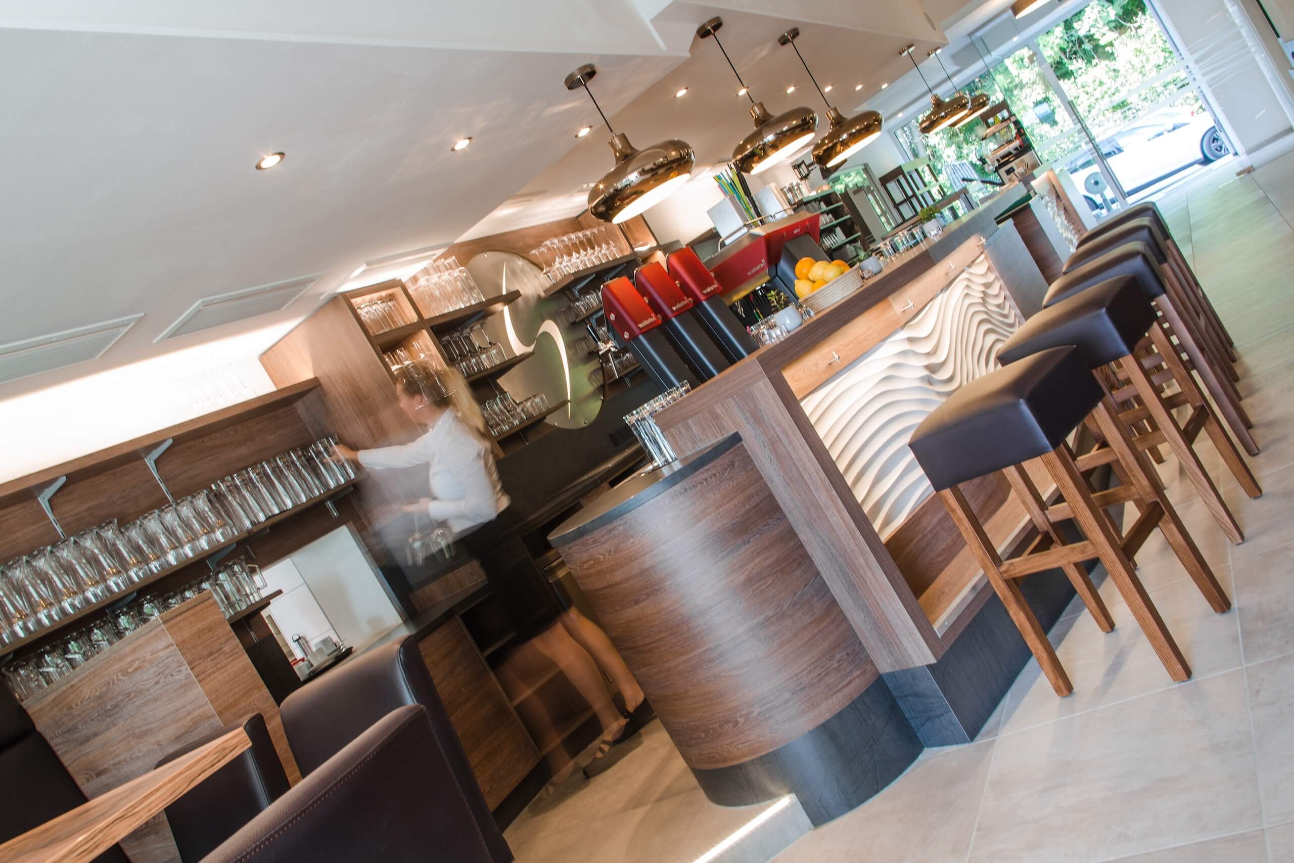 Moderne Bar mit stilvollem Holzdesign, Hockern und Bartresen, Kellner im Hintergrund.