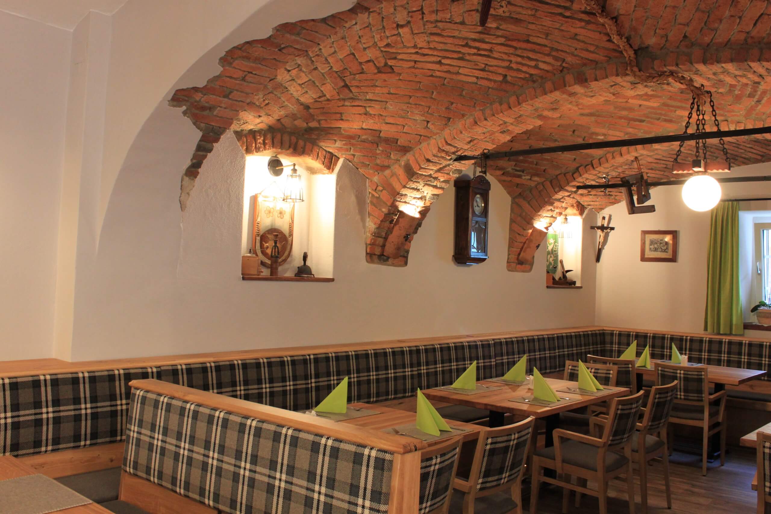 Gemütlicher Gastraum mit Ziegelgewölbe, Holztischen und karierten Bänken, ideal für traditionelle Mahlzeiten.