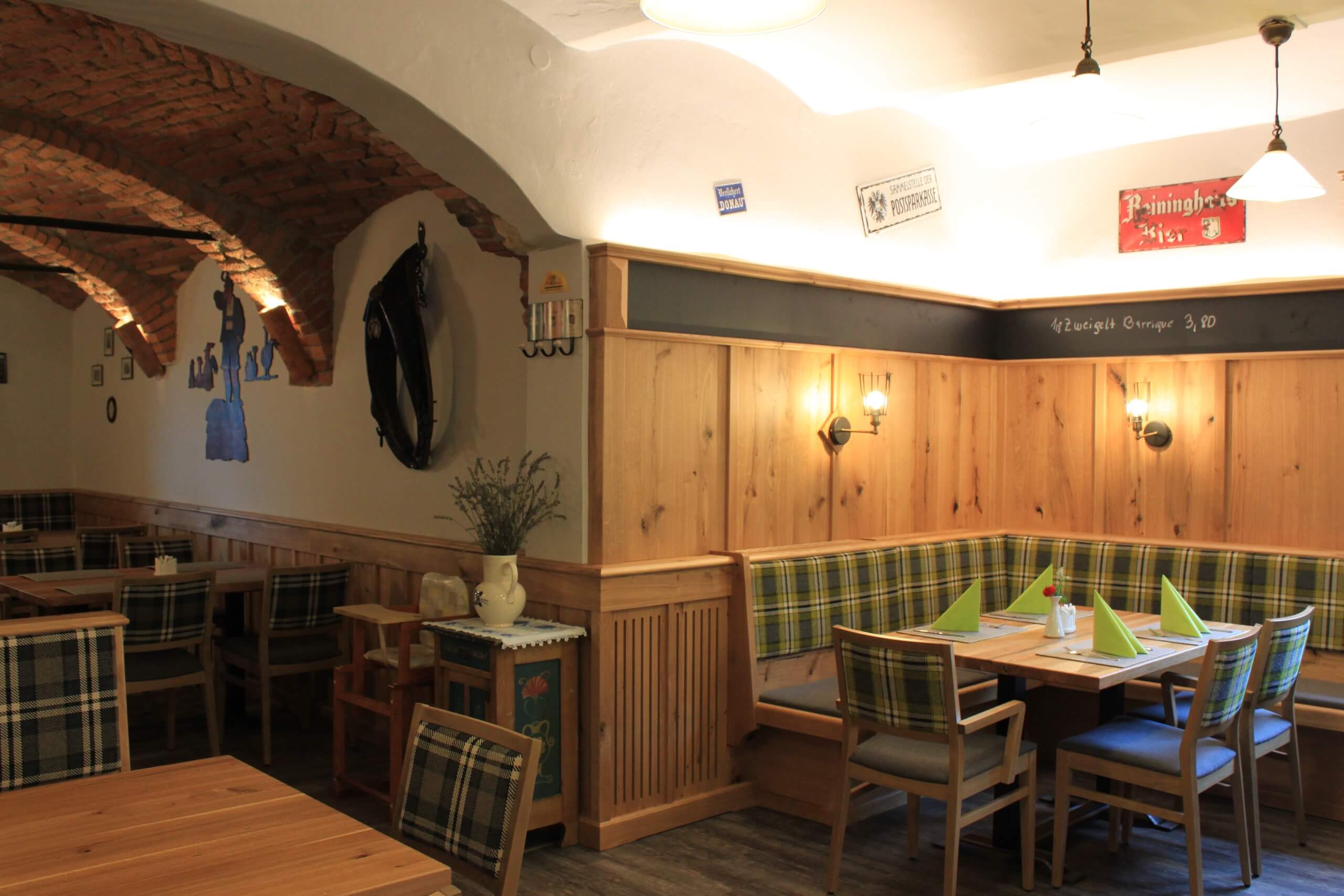 Gemütliches rustikales Restaurant mit Holzmöbeln, karierten Polstern und dekorativen Elementen an den Wänden.