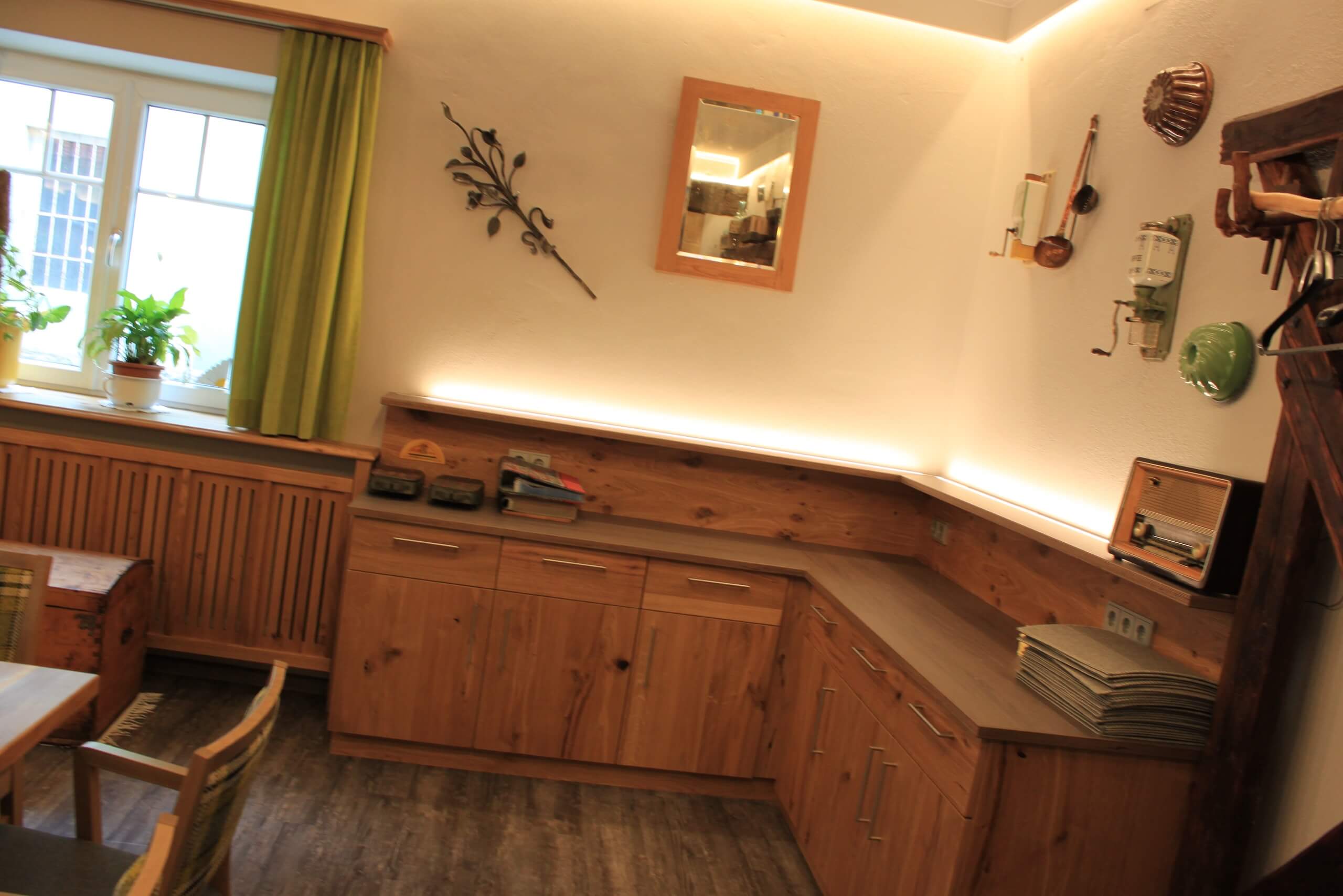 Gemütliches Wohnzimmer mit Holzmöbeln, Pflanzen am Fenster und dekorativen Elementen an den Wänden.