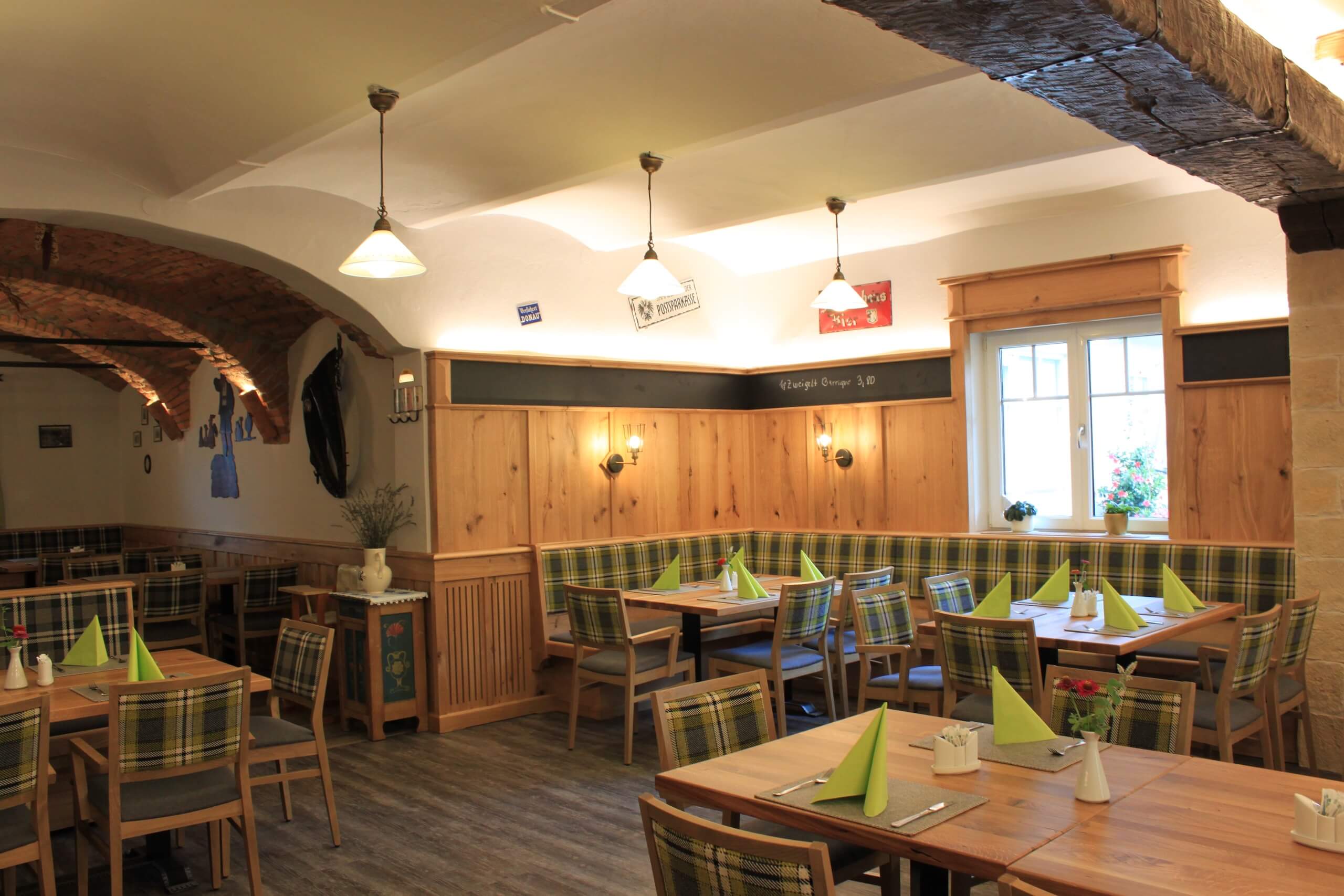 Gemütliches Restaurant mit Holzeinrichtung, karierten Polstern und gefalteten Servietten auf den Tischen.