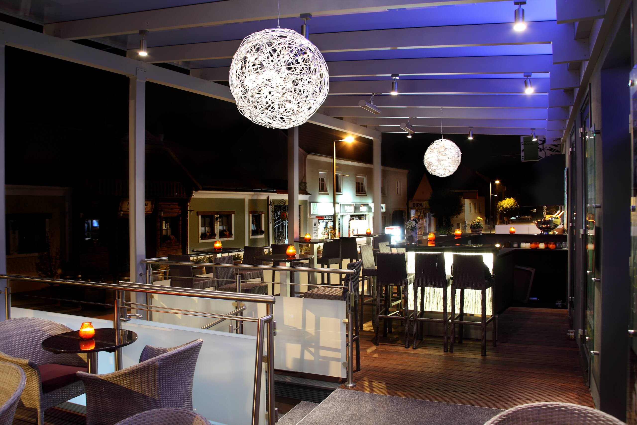Moderne Bar-Terrasse bei Nacht mit stilvoller Beleuchtung und gemütlichen Sitzgelegenheiten, ideal für Abendessen.