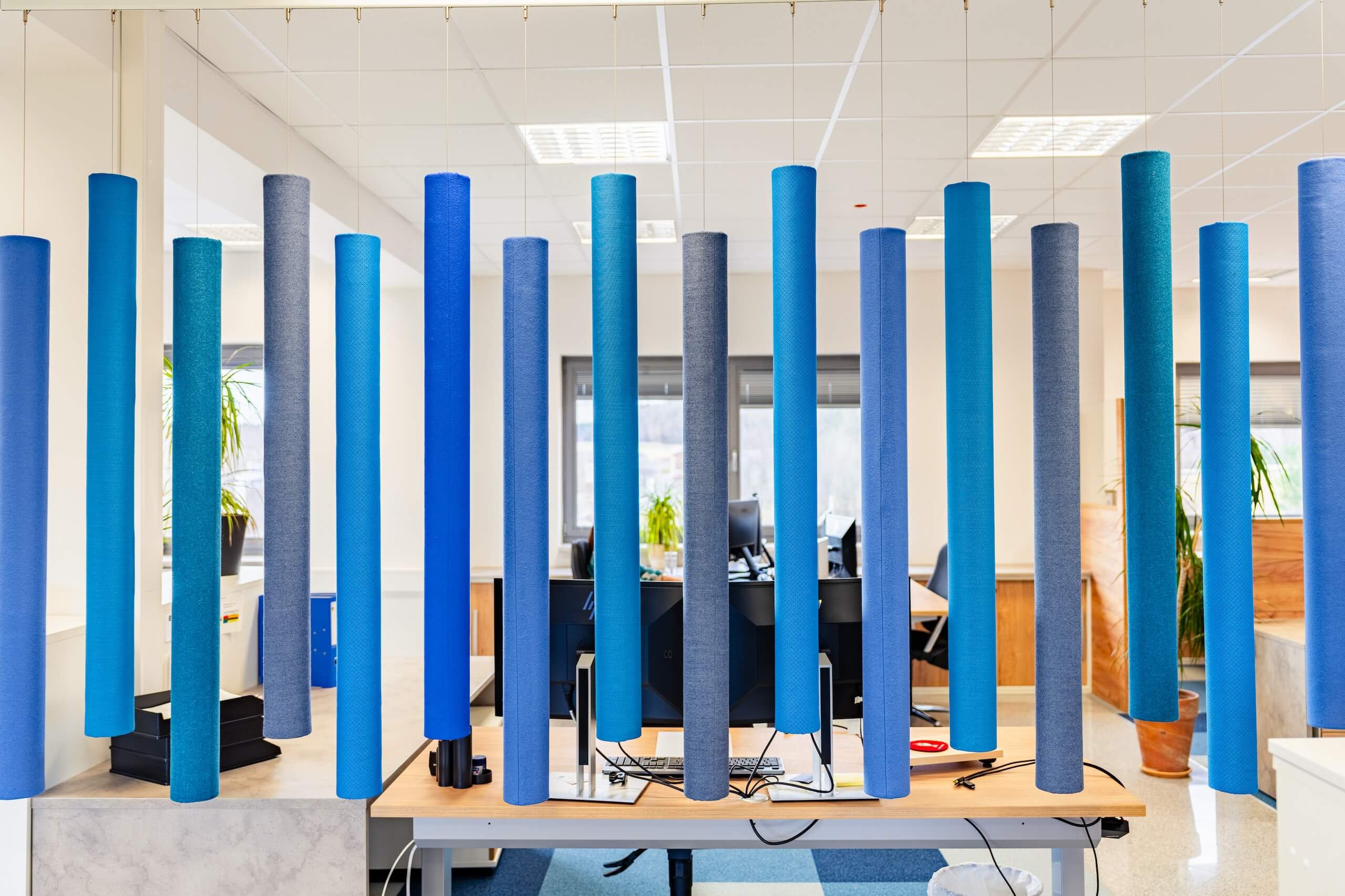 Offenes Büro mit bunten Akustikpfeilern zur Lärmdämpfung und modernem Arbeitsplatzdesign.
