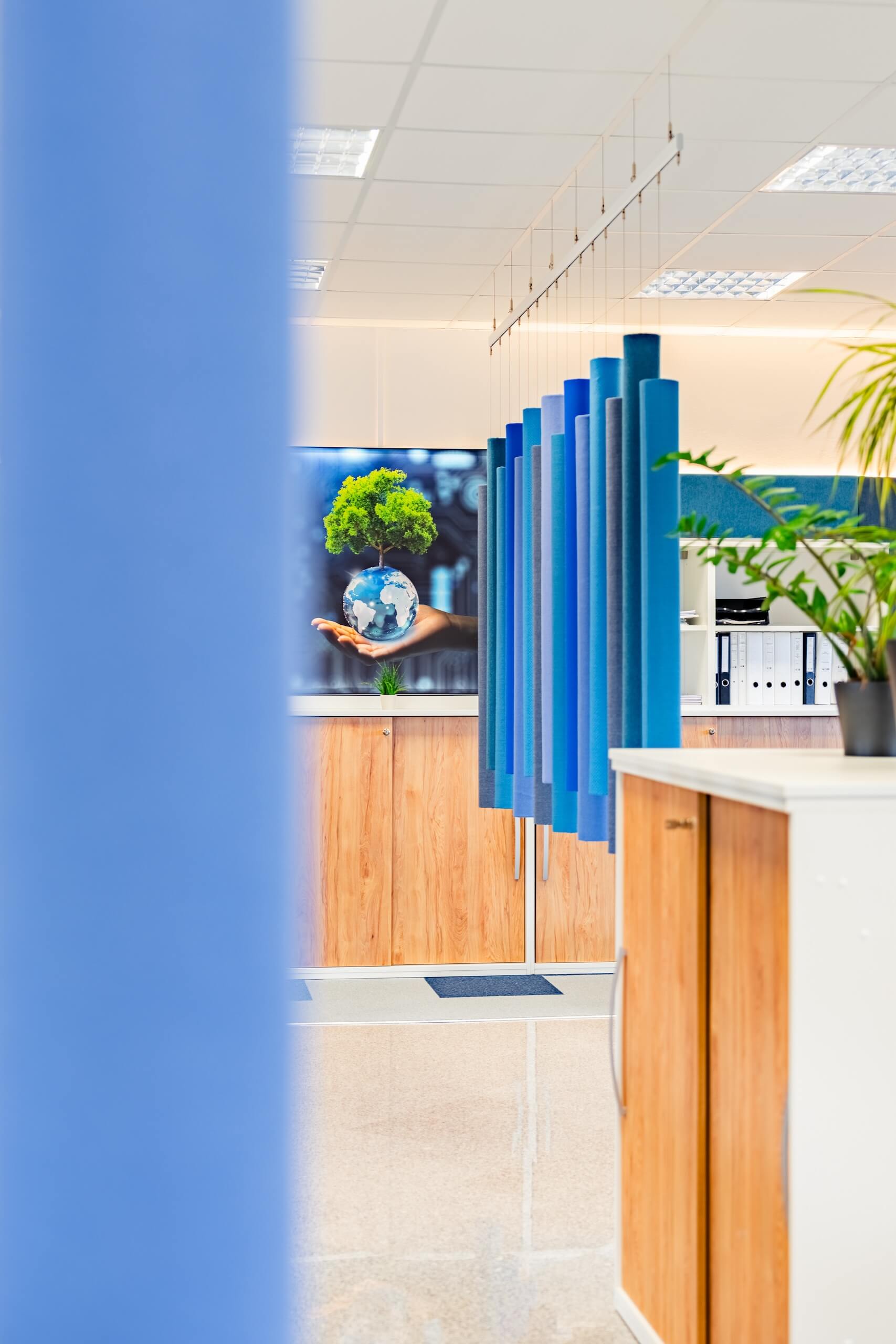 Modernes Büro mit blauem Raumtrenner und Bild von Weltkugel mit Baum, Nachhaltigkeit im Fokus.