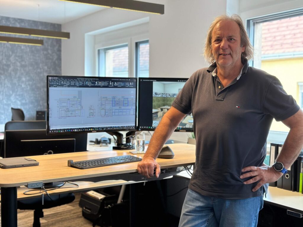 Person in einem Büro mit Computerbildschirmen, auf denen technische Zeichnungen zu sehen sind.